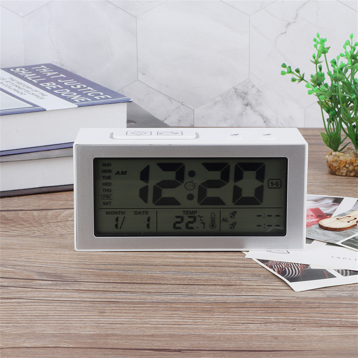 Silberne Digitaluhr zeigt Zeit und Datum auf Holztisch mit Büchern und Fotos.