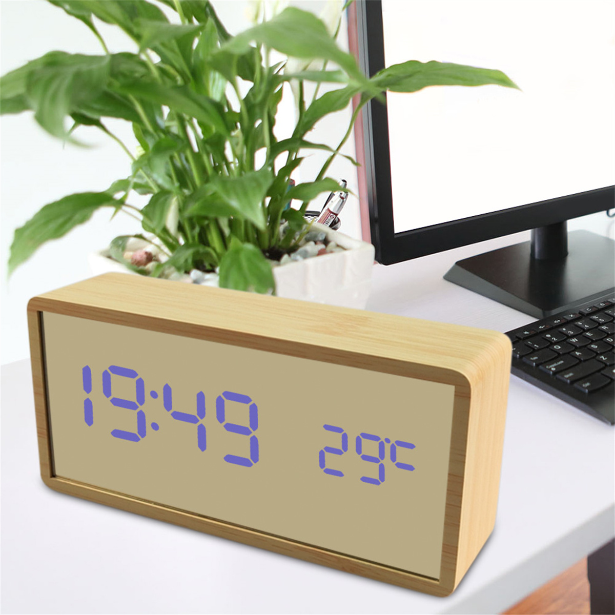 Digitaluhr aus Holz mit 19:49 und 29°C. Im Hintergrund eine Pflanze und ein Computerbildschirm.