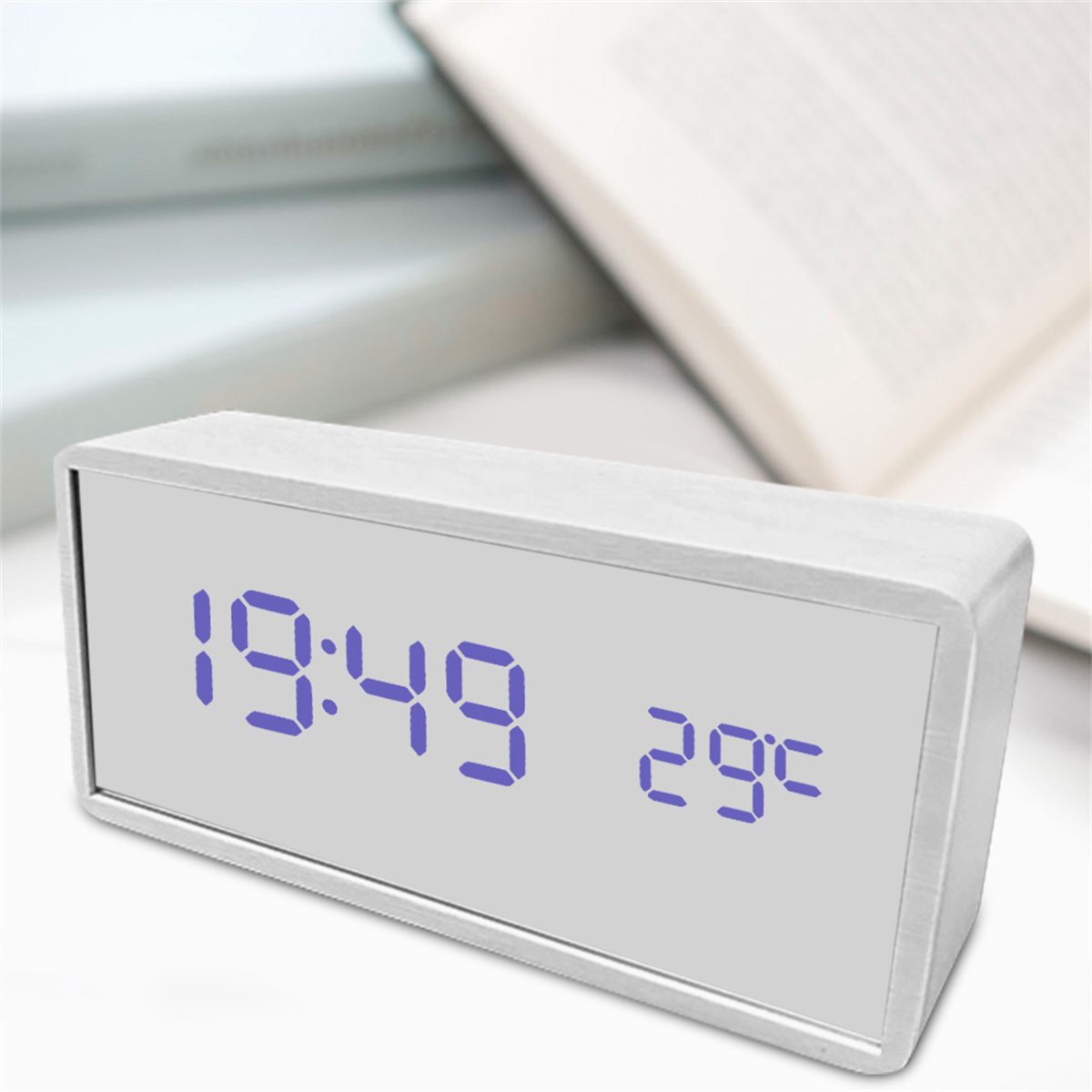 Eine weiße Digitaluhr zeigt 19:49 und 29°C an. Bücher sind im Hintergrund unscharf.