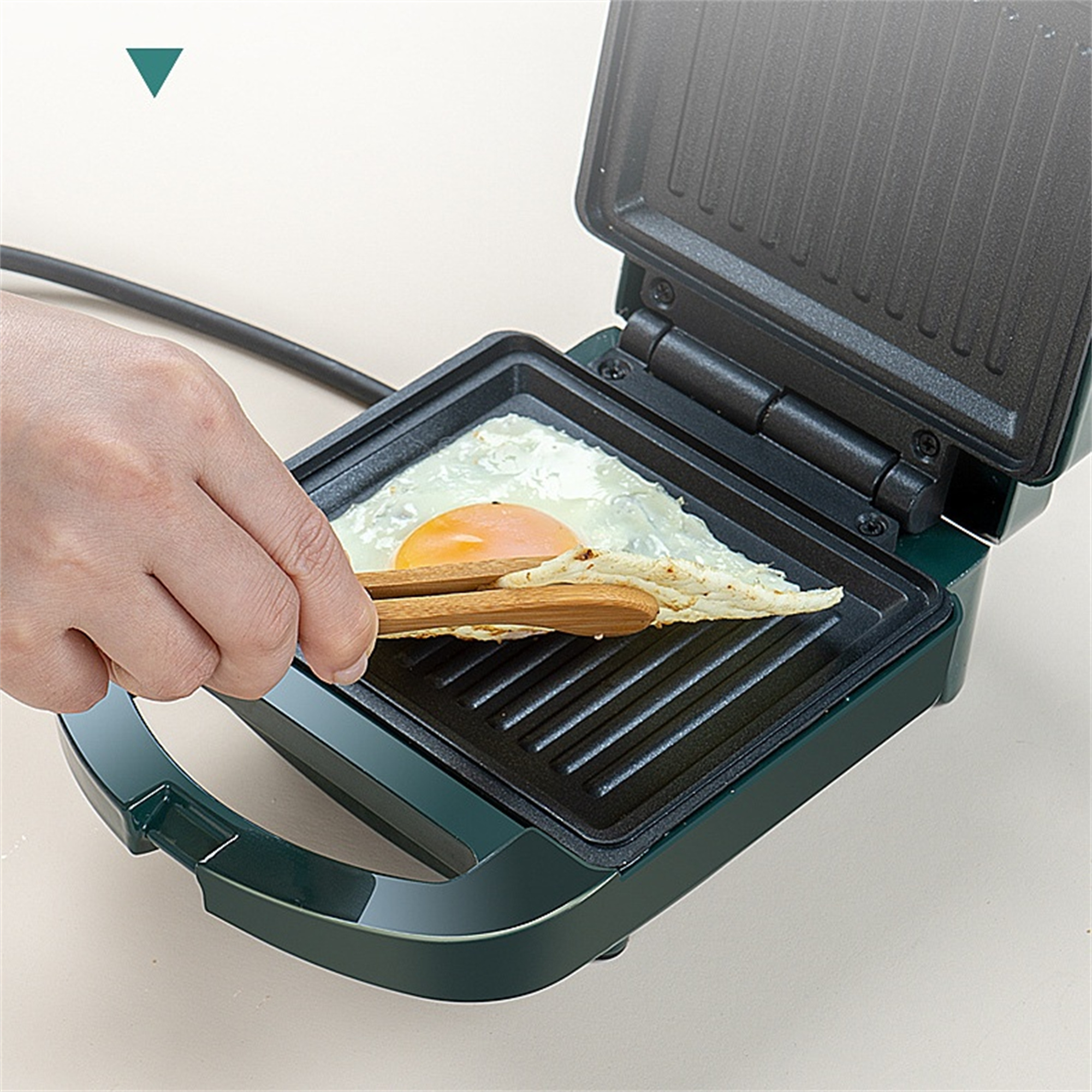 Ein Ei wird in einem Mini-Grill gebraten. Eine Zange hält ein Toaststück. Grüner Grill.