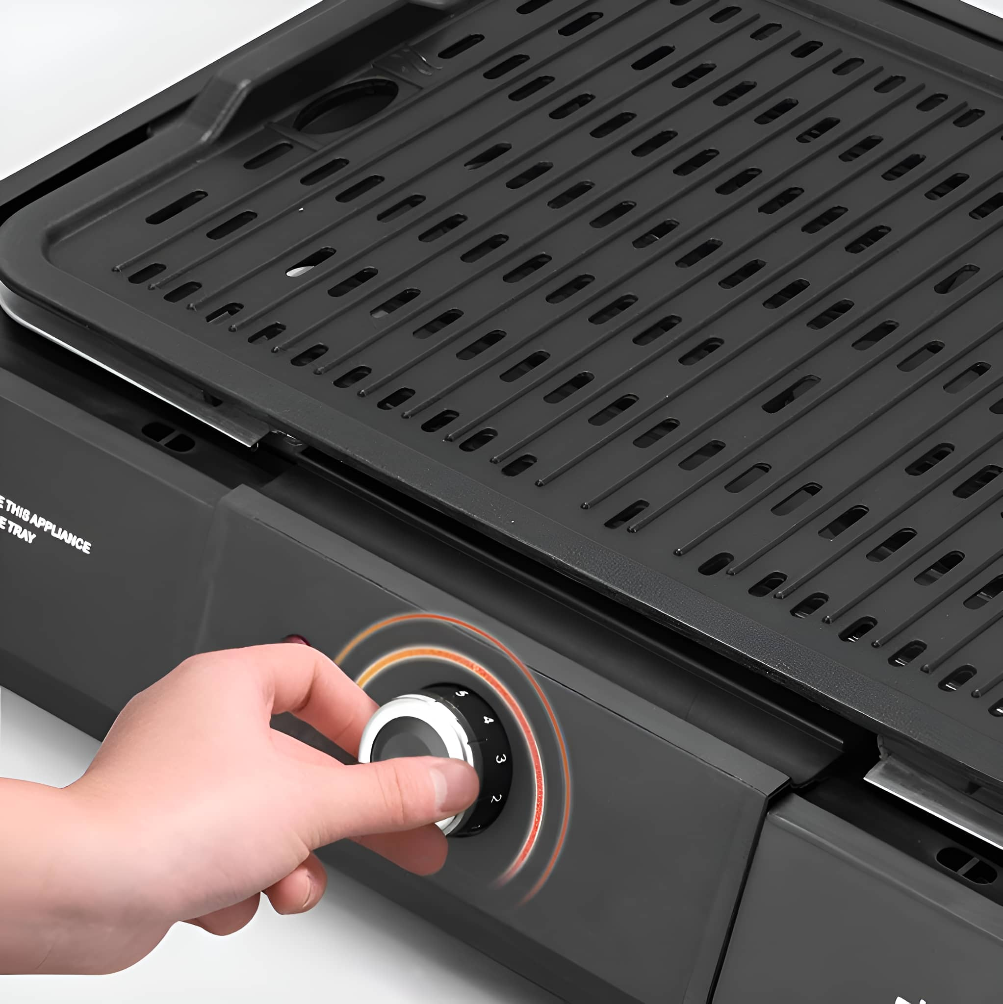 Nahaufnahme eines schwarzen Grills. Eine Hand dreht einen Drehregler. Die Oberfläche ist schwarz.