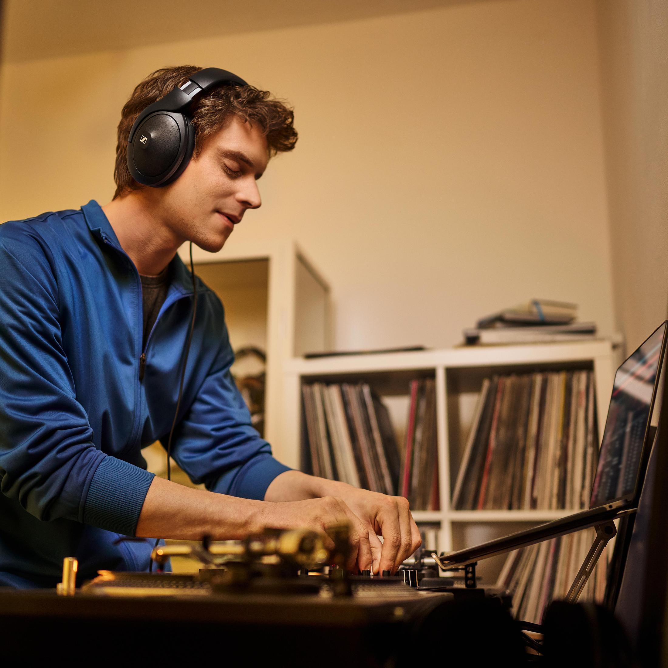 Hombre con auriculares, mezclando música en un tocadiscos. Estanterías con discos al fondo.