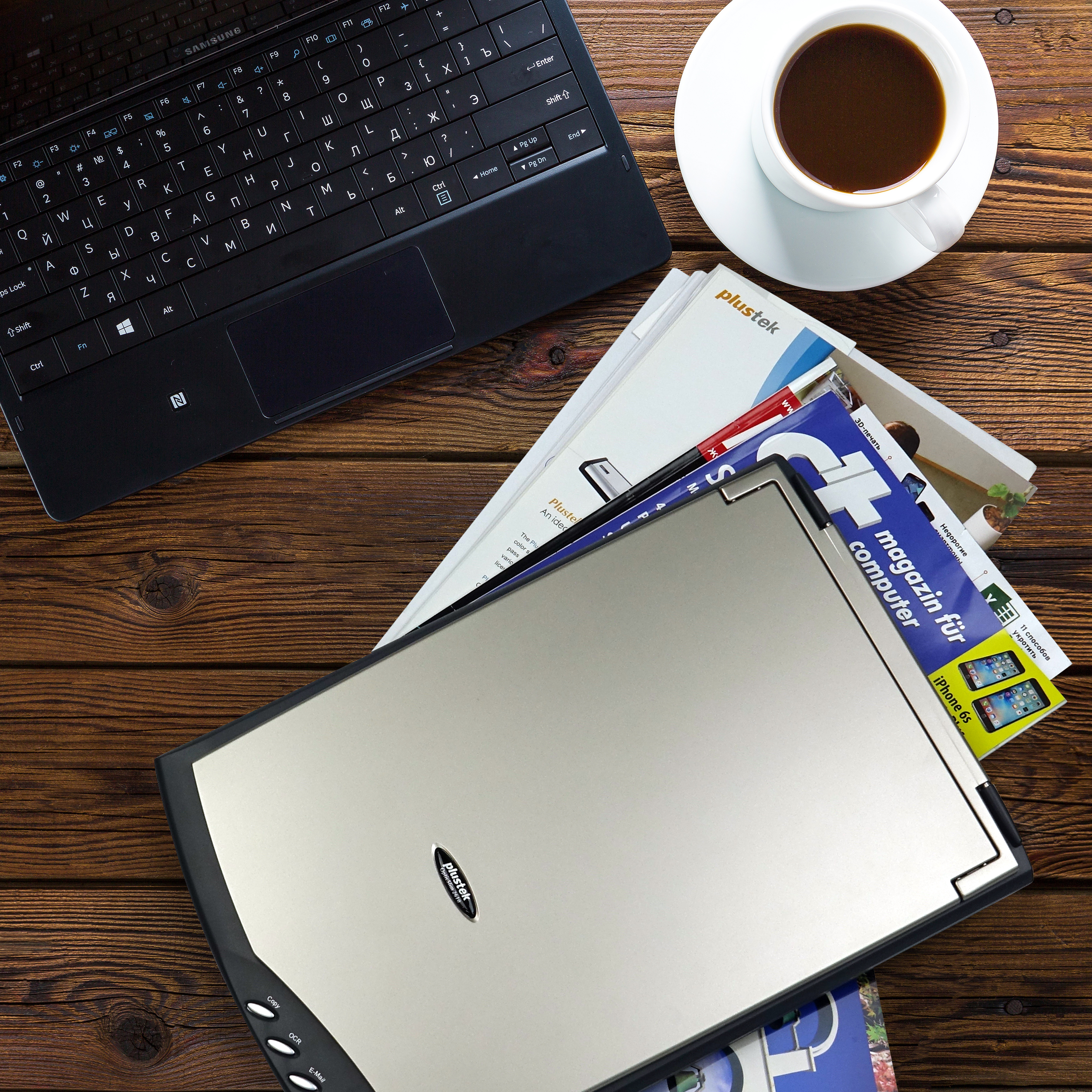 Scrivania con laptop, riviste, scanner e tazza di caffè.