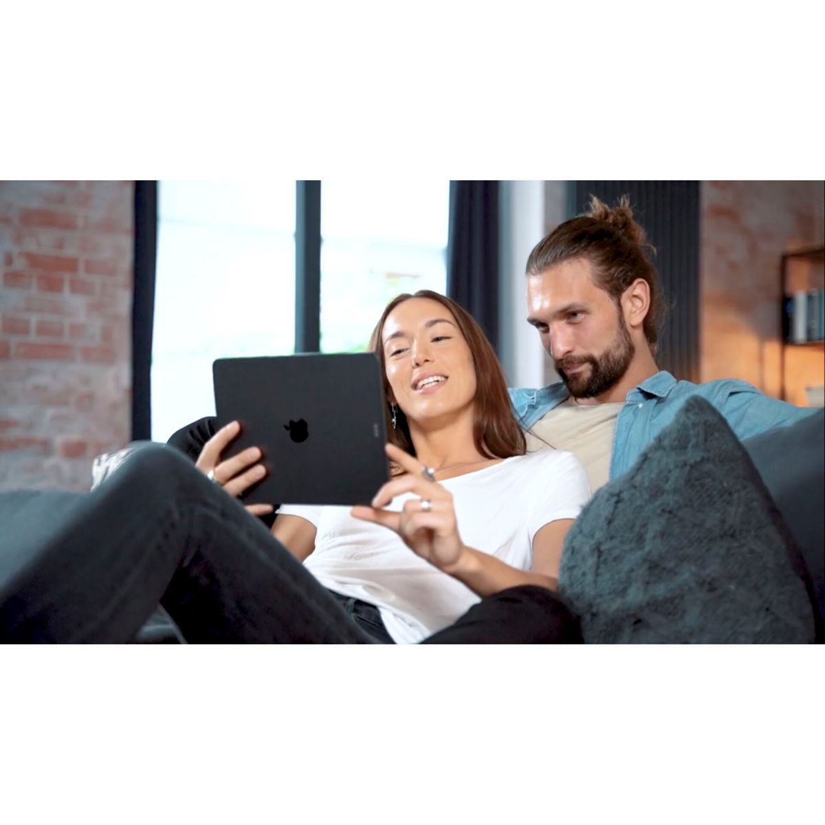 Ein Paar auf einem Sofa, das sich einen schwarzen Tablet-PC ansieht. Die Frau hält das Tablet.
