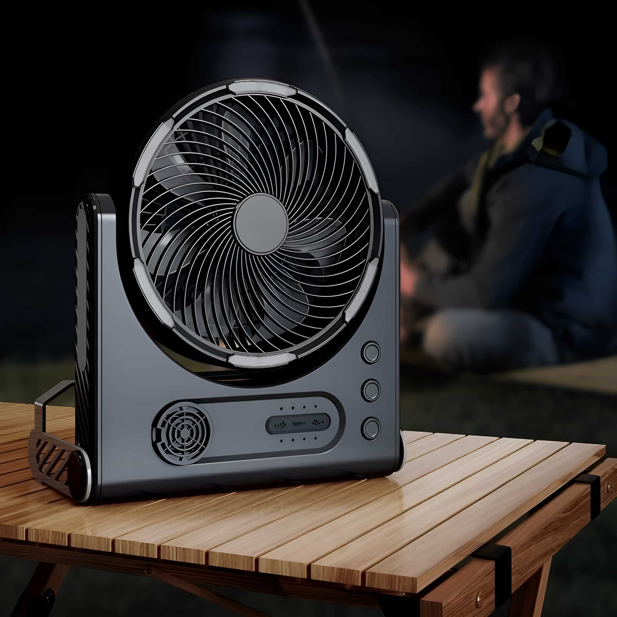 Schwarzer Ventilator auf einem Holztisch mit einem Mann im Hintergrund, der sich am Lagerfeuer aufhält. Nachtszene.