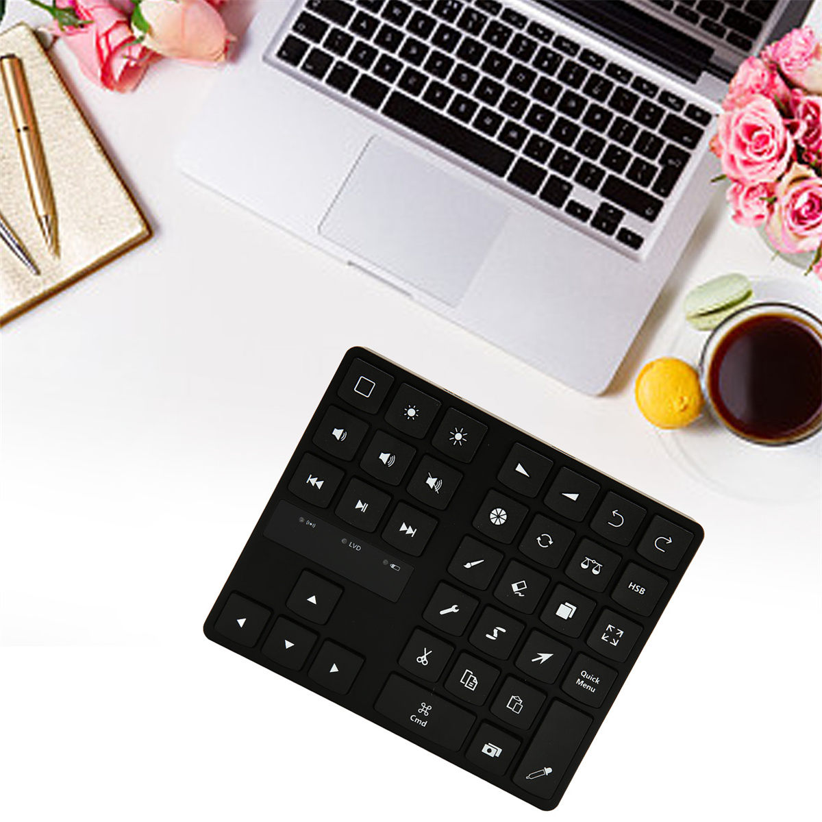 Eine schwarze Tastatur auf einem weißen Schreibtisch mit Laptop, Blumen und einer Tasse Kaffee.