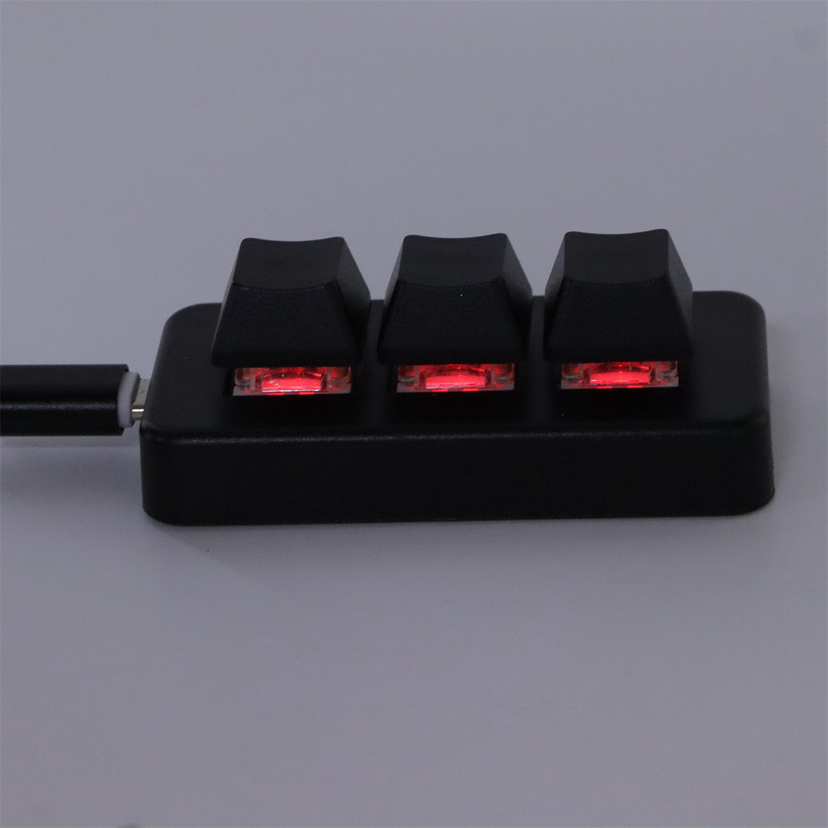 Eine schwarze mechanische Tastatur mit drei rot hinterleuchteten Tasten auf grauer Oberfläche.