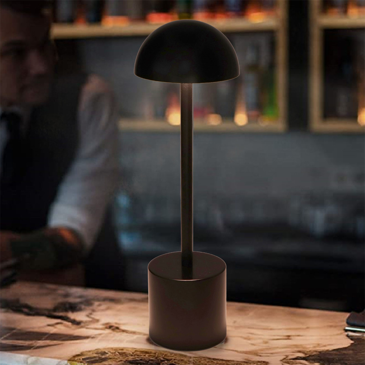 Schwarze, kuppelförmige Lampe auf einer Bar. Die Lampe hat einen langen Stiel und steht auf einem Zylindersockel.