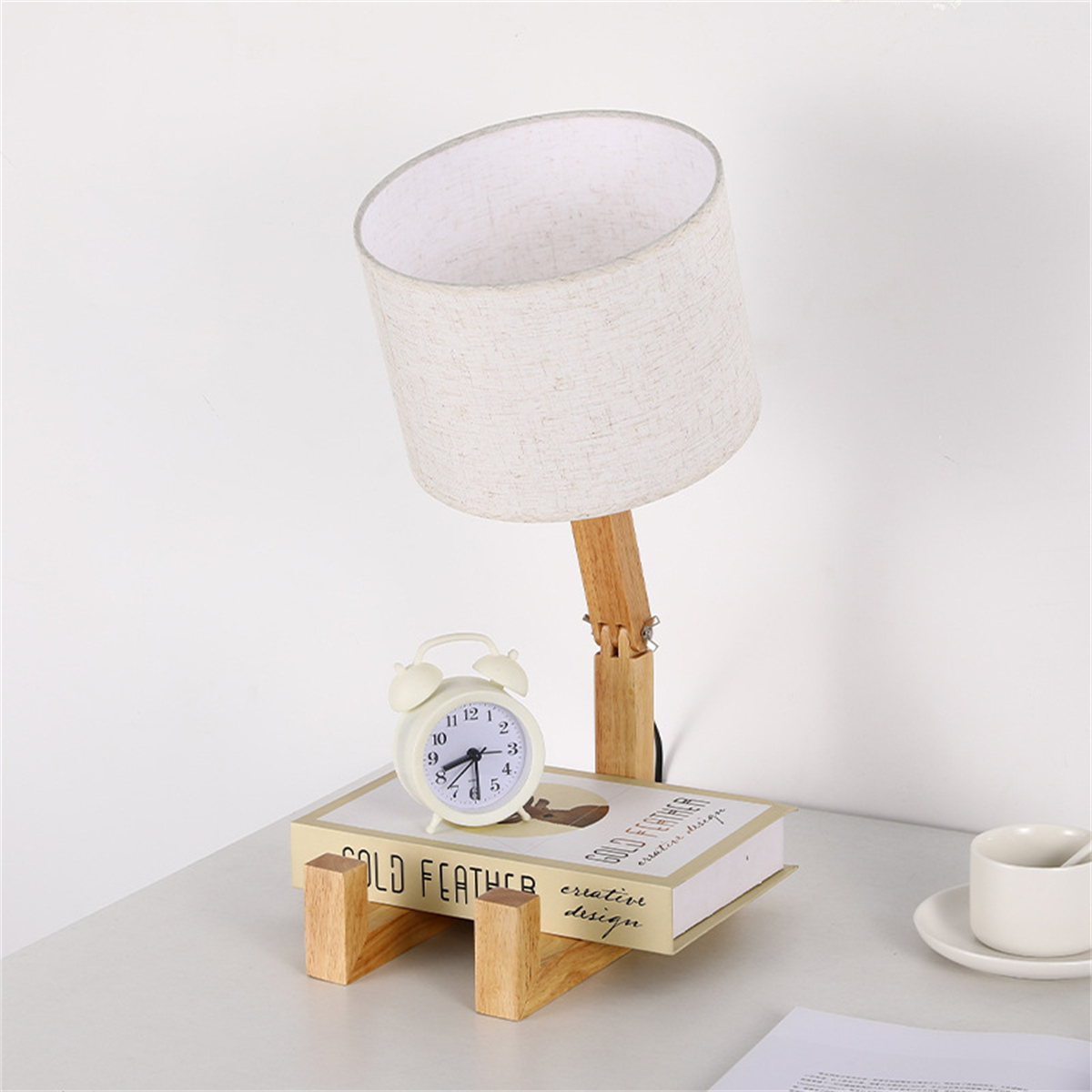 Eine Schreibtischlampe, ein Wecker und ein Buch auf einem Schreibtisch. Der Hintergrund ist weiß.