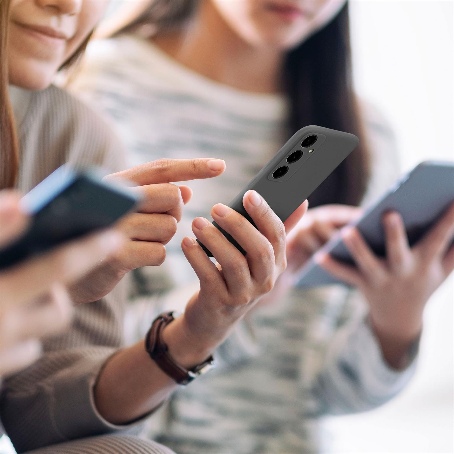 Drei Personen benutzen Smartphones. Zwei halten Telefone, eine Person hält ein Telefon in einer schwarzen Hülle.
