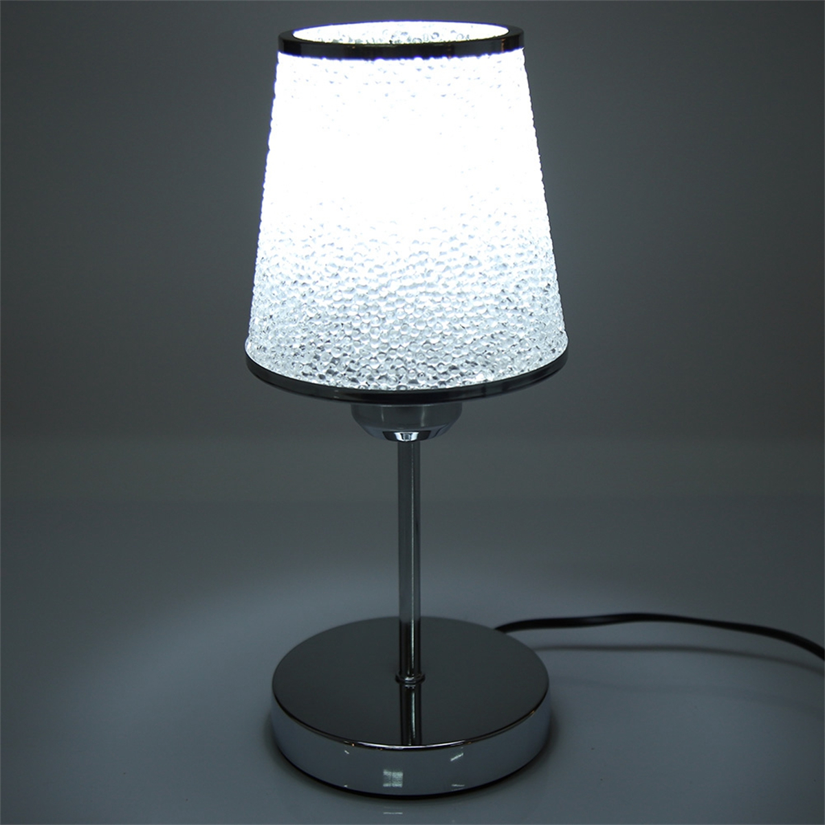 Eine beleuchtete Tischlampe mit weißem Schirm und silbernem Fuß.