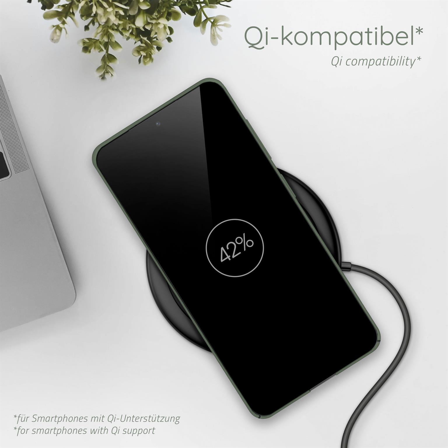 Telefon auf kabellosem Ladegerät, 42% Akku. Grüne Handyhülle. Weiße Oberfläche mit Pflanzen.