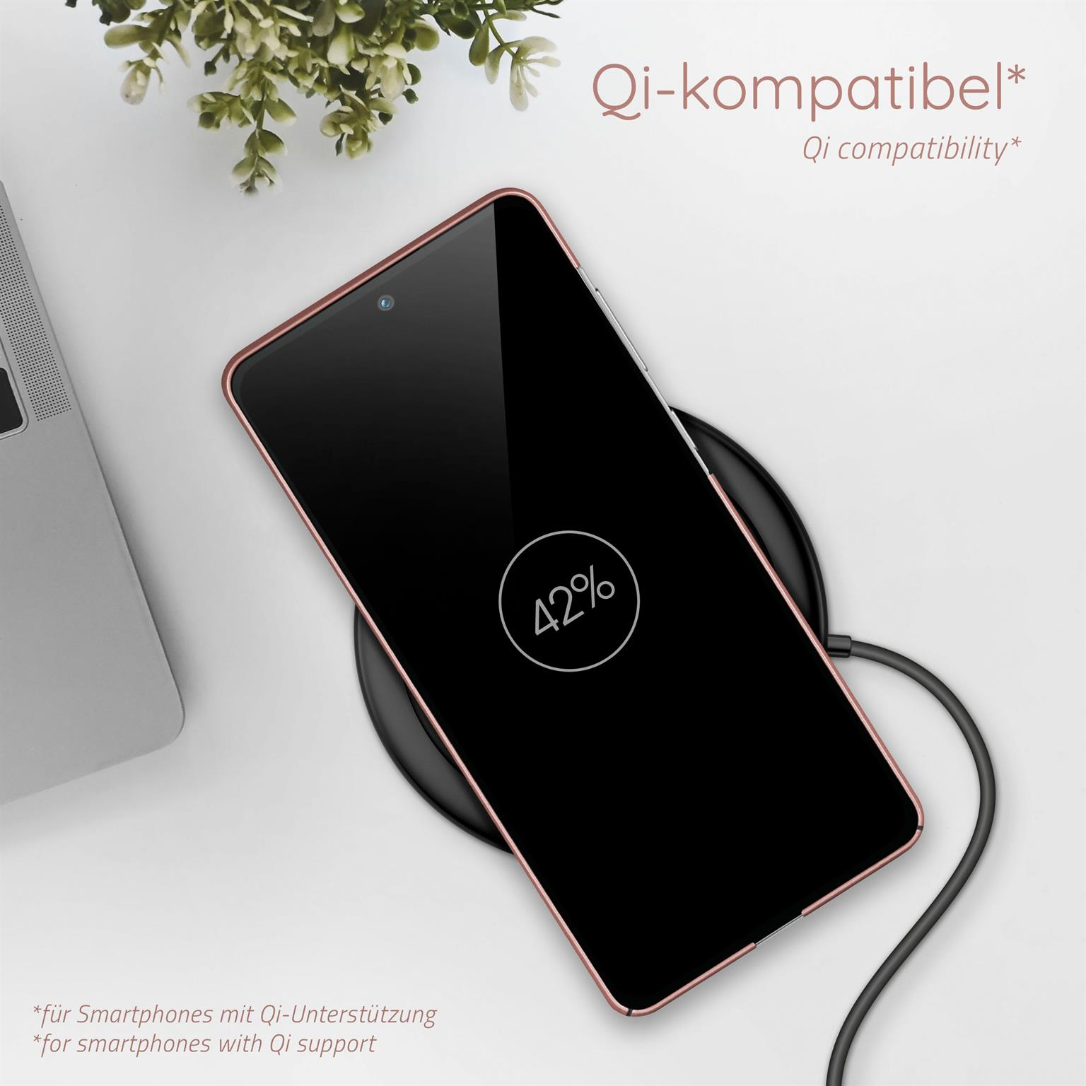 Ein Smartphone mit Ladebildschirm auf einem kabellosen Ladegerät, im Hintergrund ein Laptop.