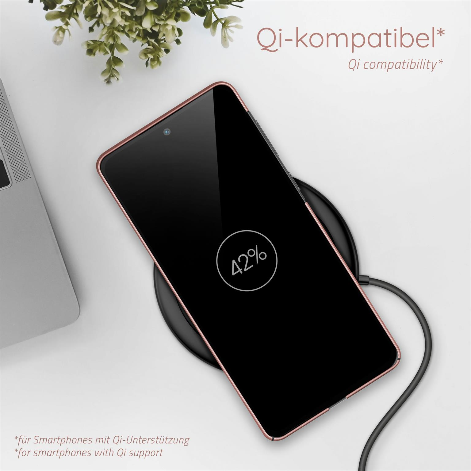 Ein Telefon, das drahtlos auf einem Pad geladen wird, zeigt eine 42% Ladung, in der Nähe eines Laptops.