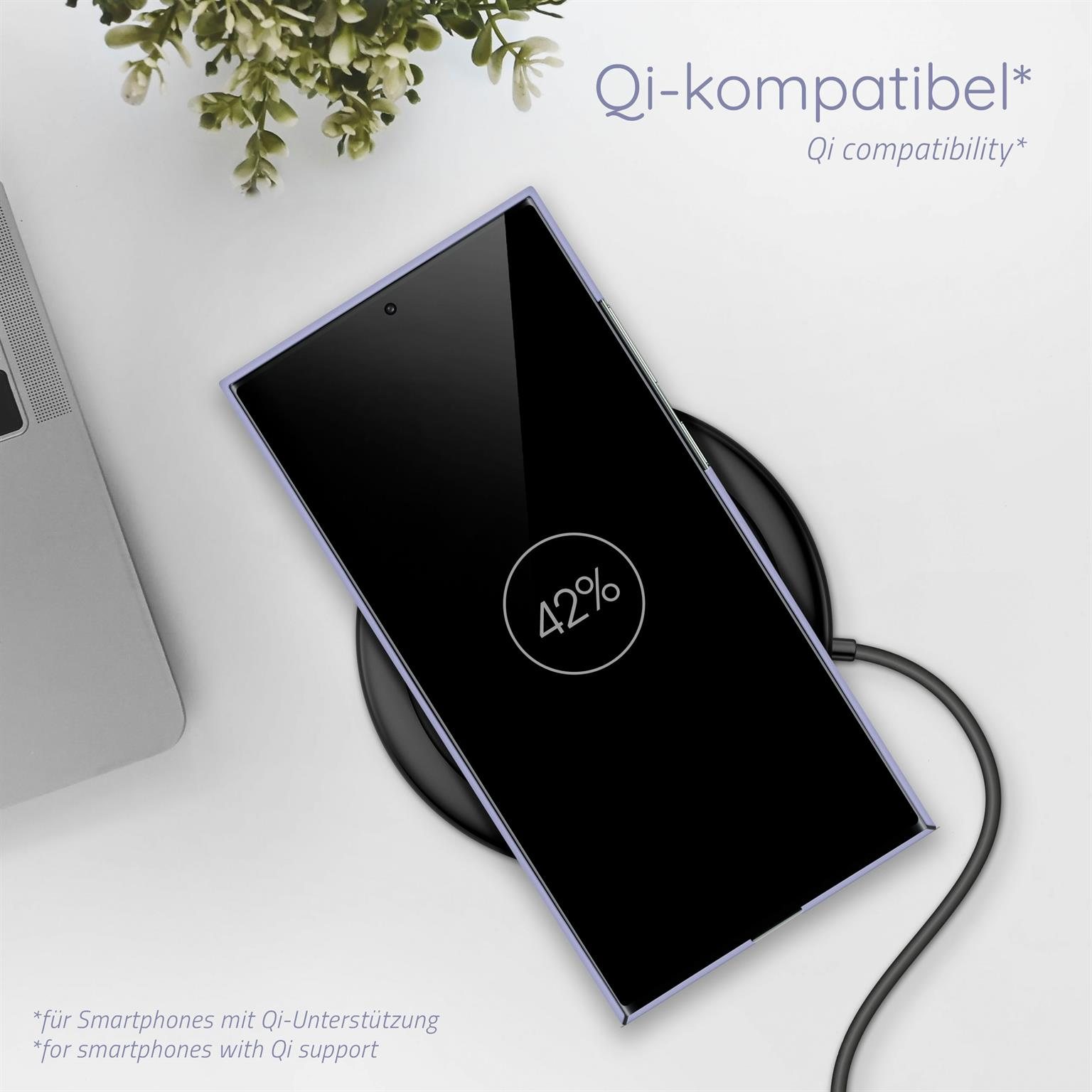 Ein Telefon auf einem Ladepad, zeigt 42 % Ladung an. Ein Laptop und eine Pflanze im Hintergrund.