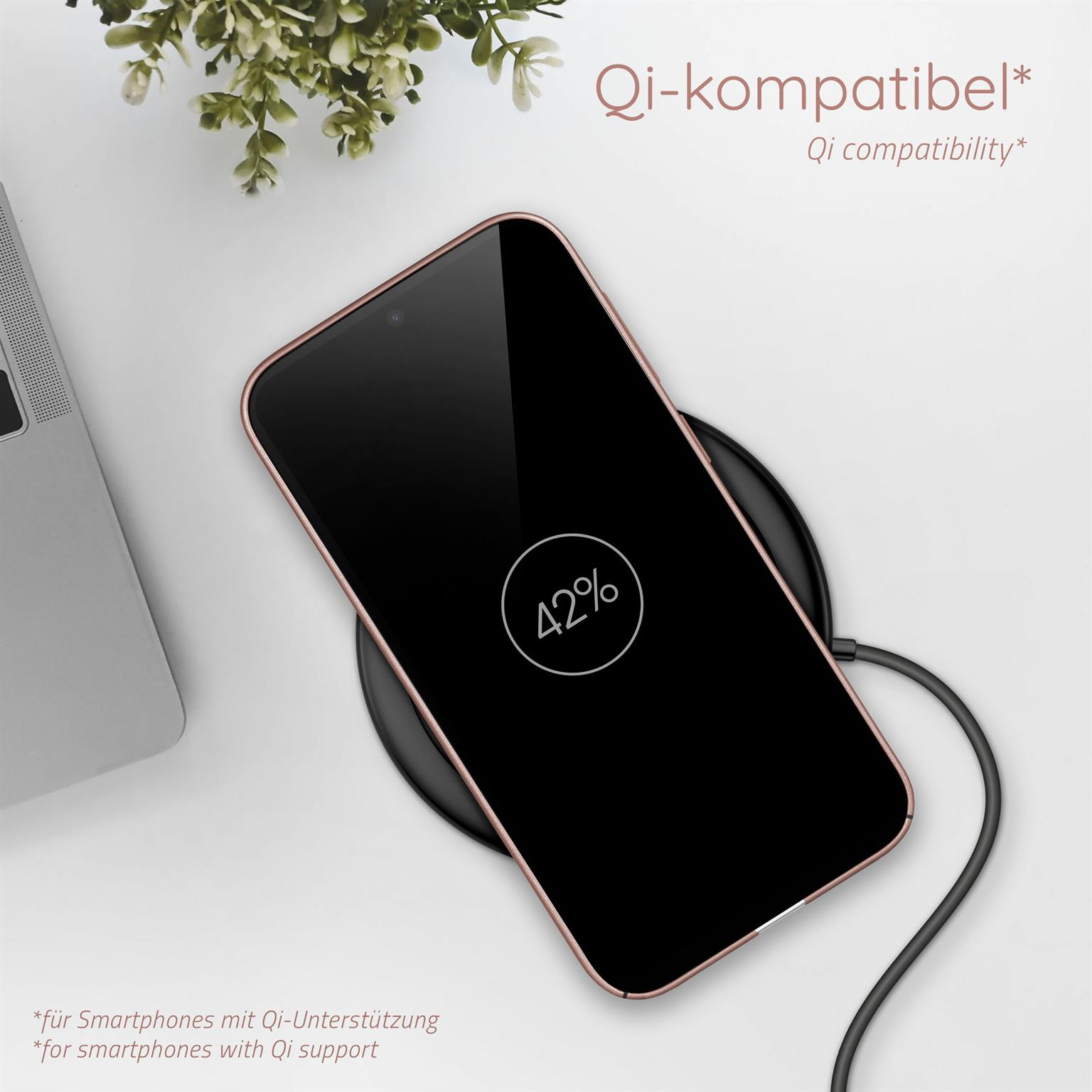 Ein Telefon, das auf einem kabellosen Ladegerät geladen wird. Der Bildschirm zeigt '42%'. Pflanze und Laptop im Hintergrund.