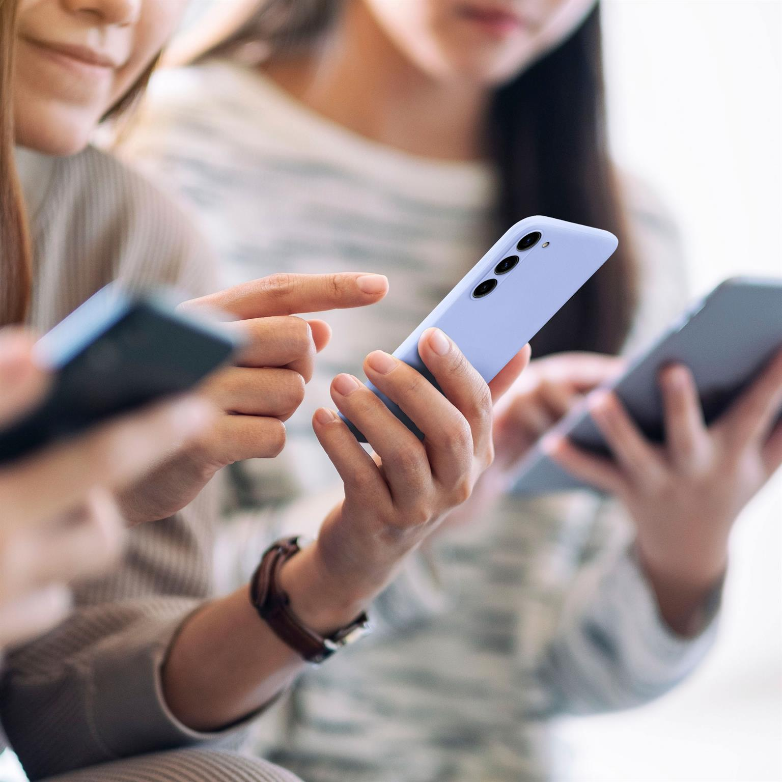 Drei Frauen halten Smartphones, zeigen und schauen auf die Bildschirme. Die Telefone sind hellblau.