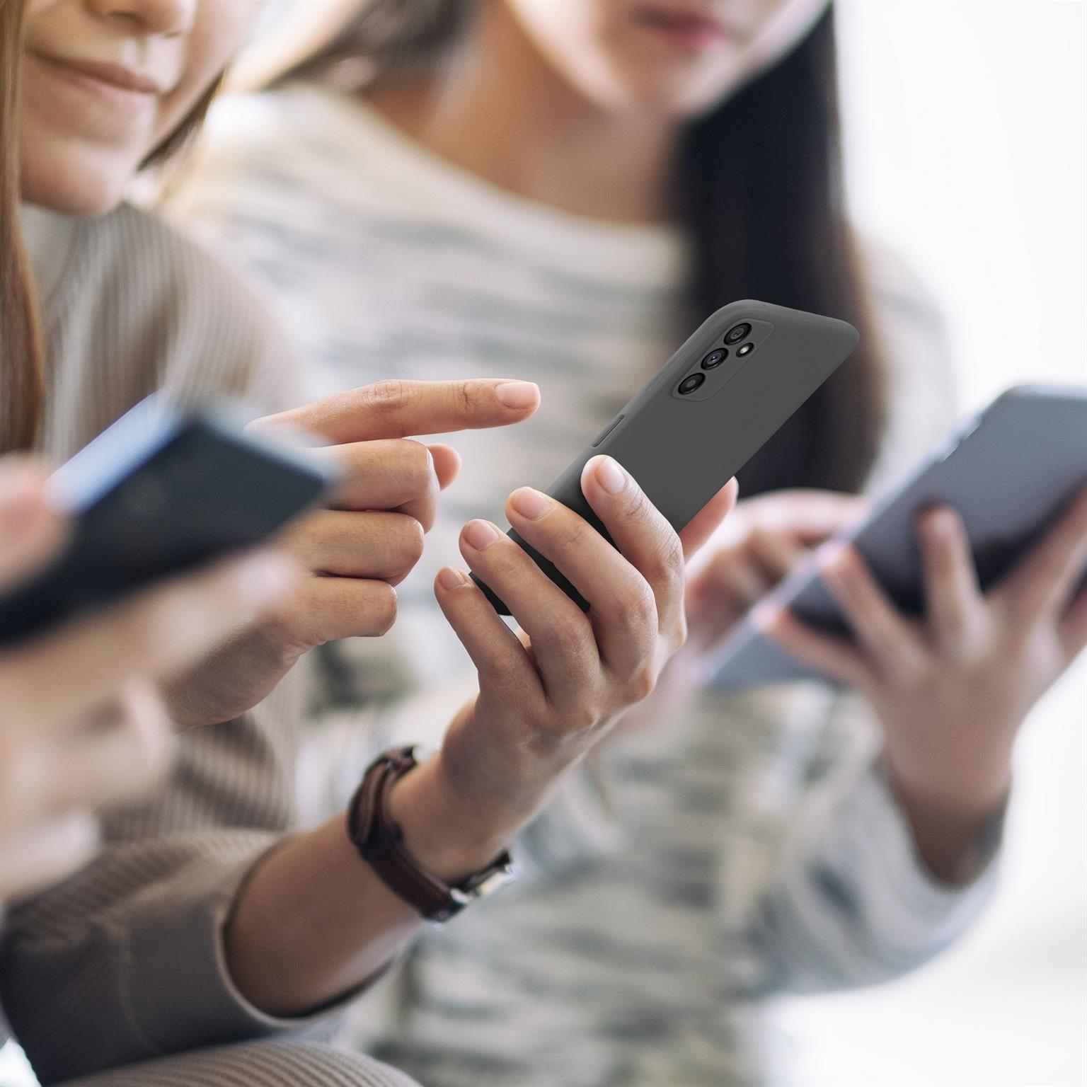 Drei Frauen benutzen Handys, eine hält ein Handy in einer schwarzen Hülle. Verschwommener Hintergrund.