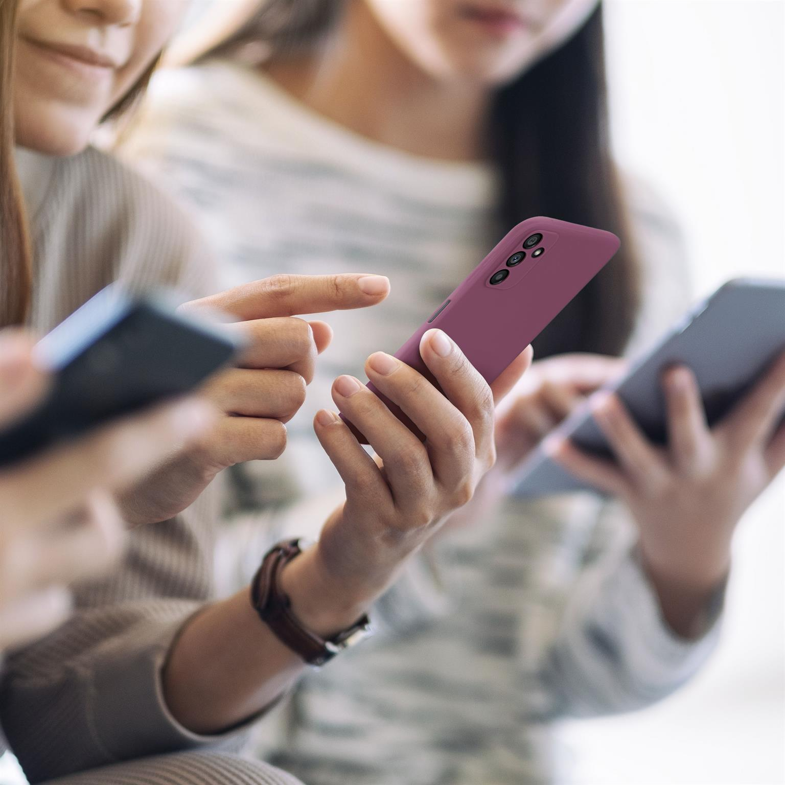 Drei Personen halten Smartphones mit lilafarbener Hülle. Nahaufnahme.