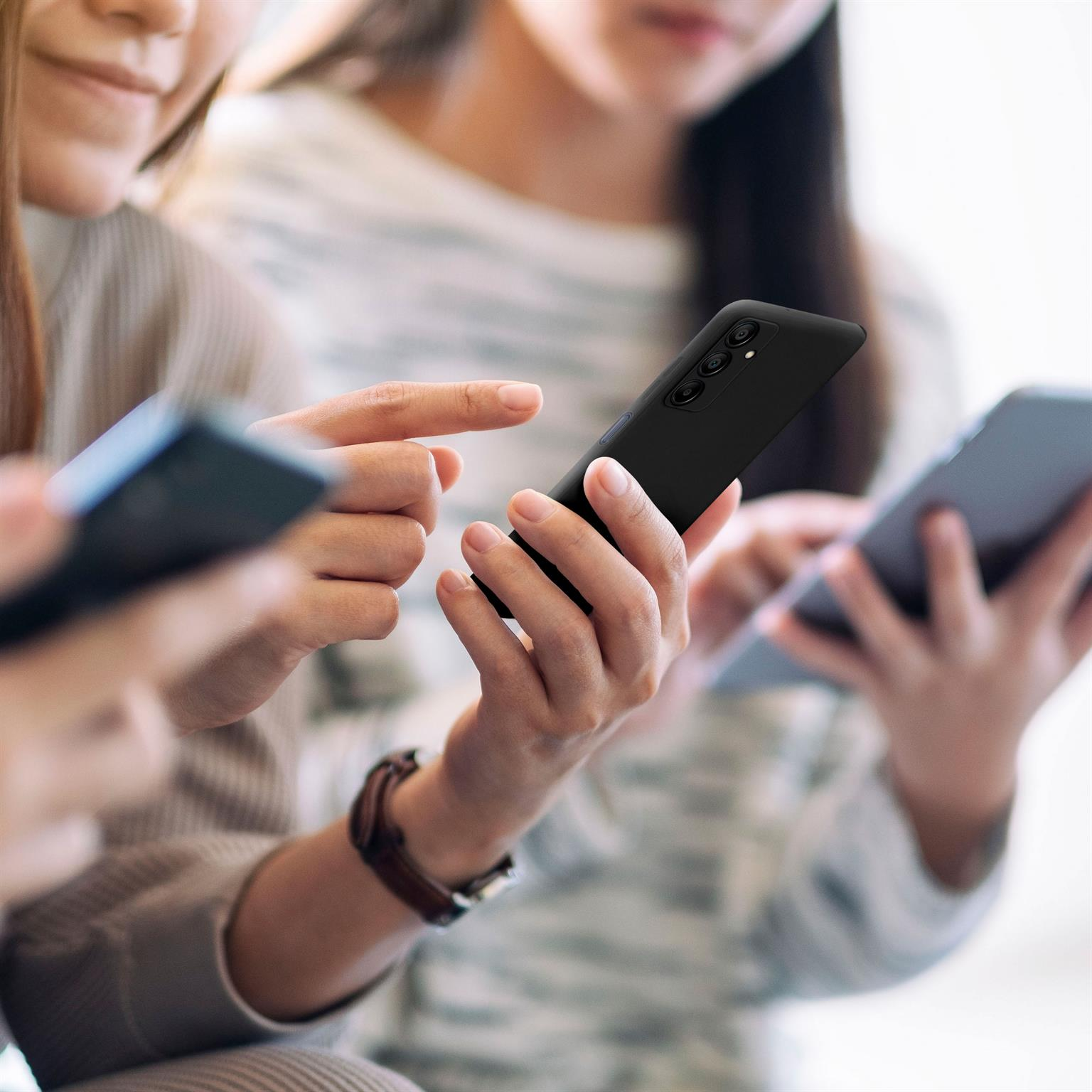 Drei Personen halten Telefone, zwei im Fokus, eine schwarze Handyhülle, die andere blau.