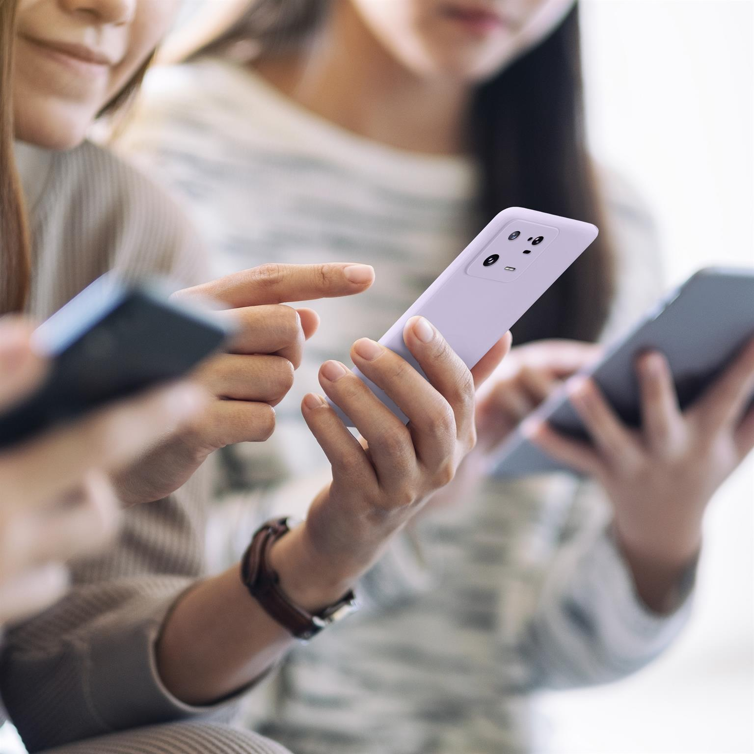 Drei Personen halten Telefone. Eines ist in einer lilafarbenen Hülle. Ihre Gesichter sind teilweise sichtbar.