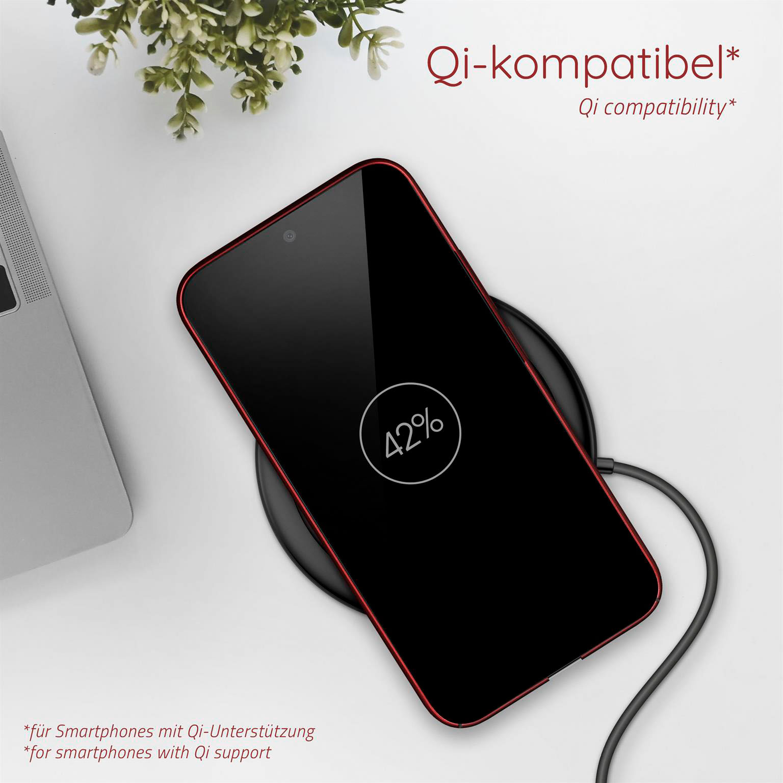 Telefon lädt auf kabellosem Pad. Schwarzer Bildschirm mit 42 %. Pflanze und Laptop im Hintergrund.
