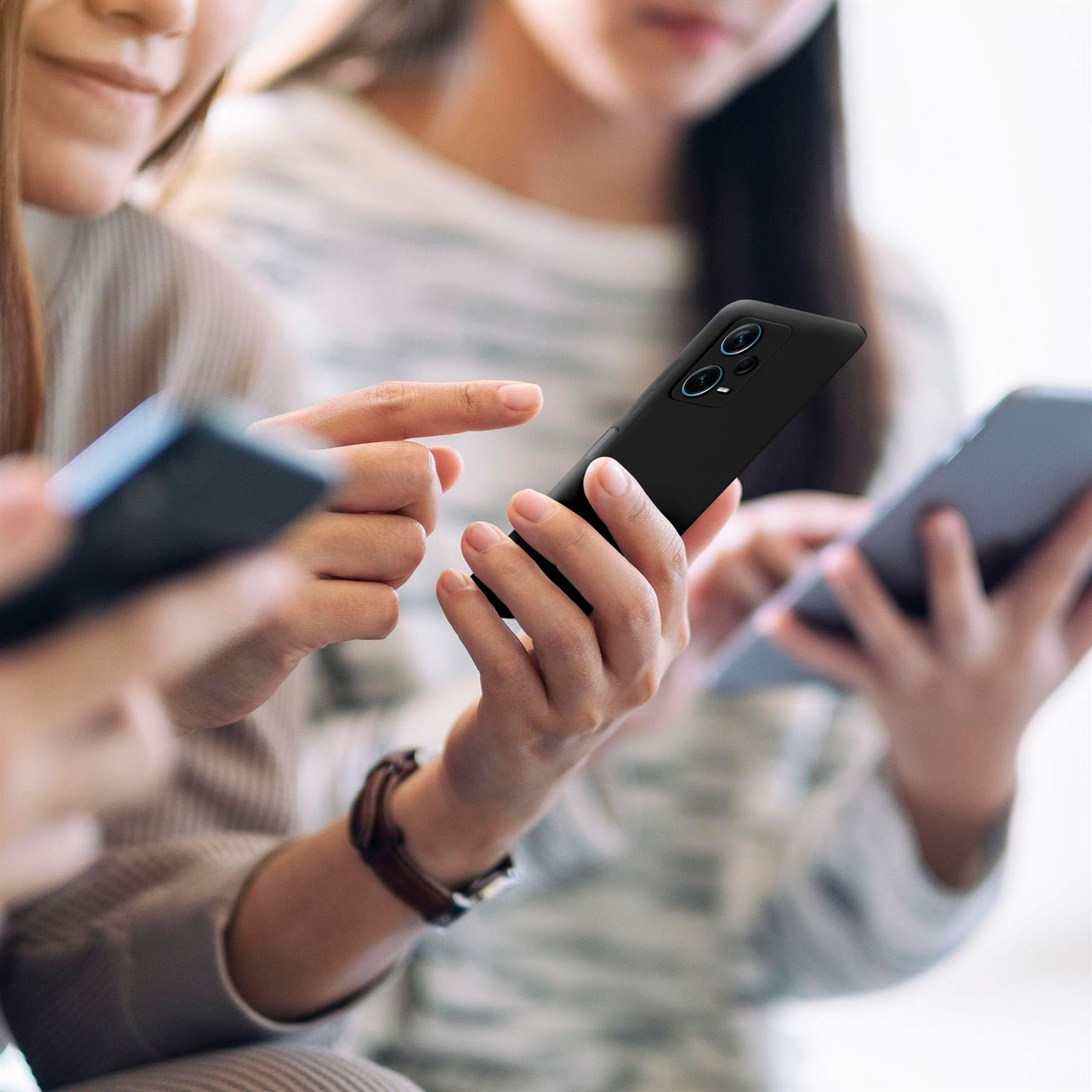 Drei Personen halten Telefone, eine schwarze Handyhülle ist sichtbar.