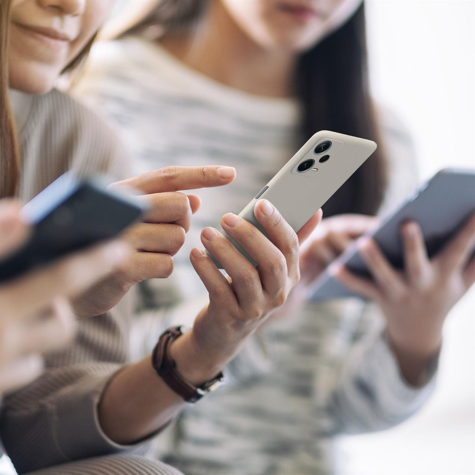 Drei Personen benutzen Smartphones. Einer hält ein hellgraues Telefon, andere dunkle Telefone.