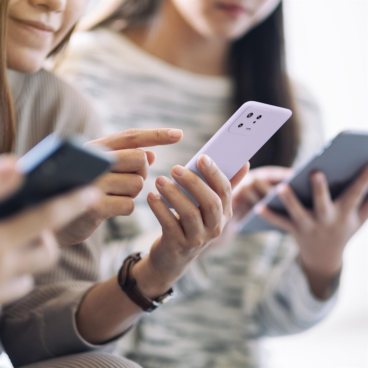 Personen halten Telefone, eine Person zeigt auf den Bildschirm. Hintergründe sind unscharf.
