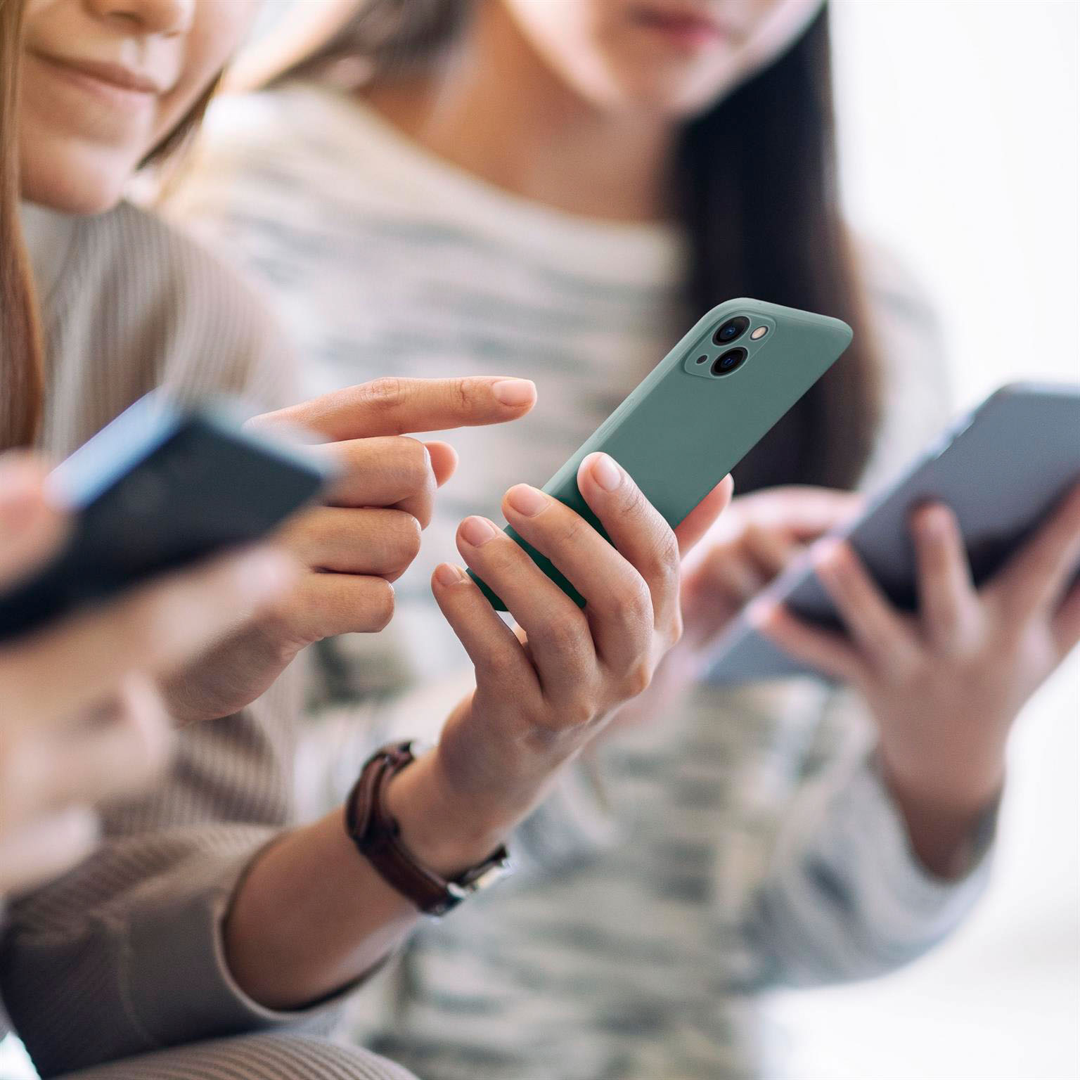 Drei Personen benutzen Smartphones. Telefone sind verschiedenfarbig. Fokus auf grünem Telefon in Händen.
