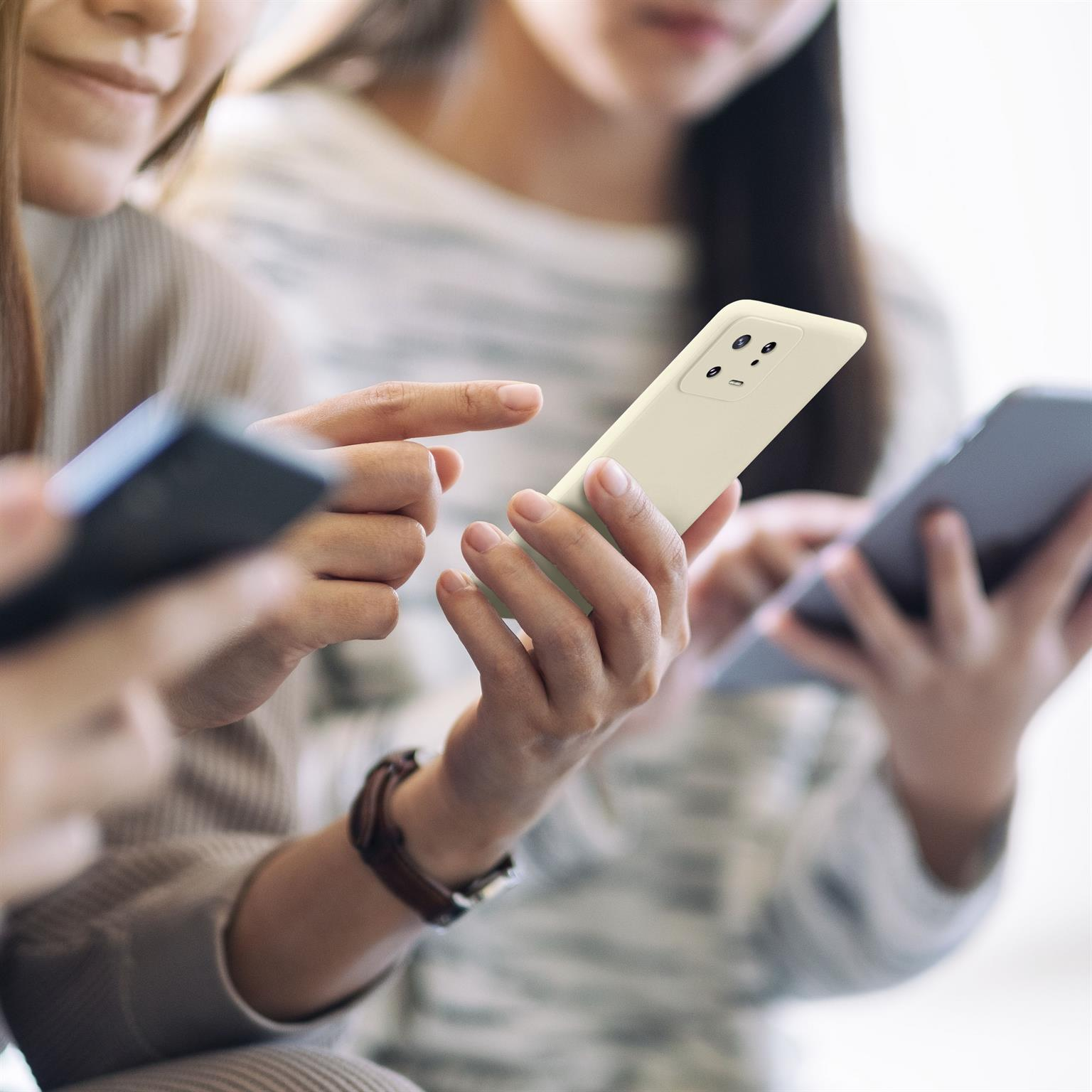 Drei Personen halten Telefone. Die Telefone sind weiß. Der Hintergrund ist verschwommen.