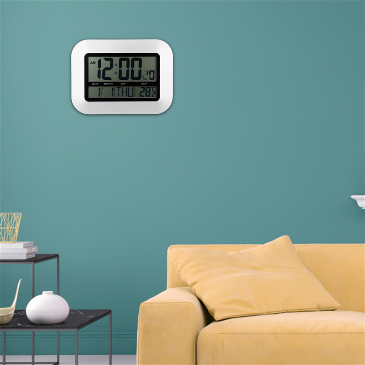 Weiße Digitaluhr an einer türkisblauen Wand. Sie zeigt 12:00 Uhr an. Eine gelbe Couch und ein Beistelltisch sind im Bild.