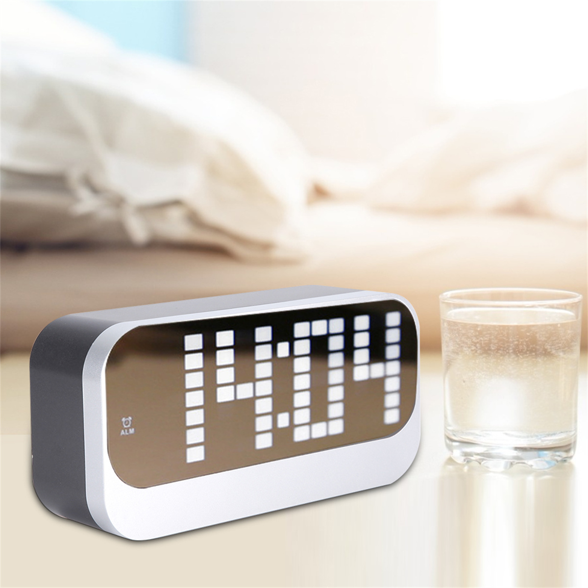 Digitaluhr auf einem Nachttisch, die 14:04 anzeigt. Ein Glas Wasser steht daneben. Verschwommener Hintergrund.