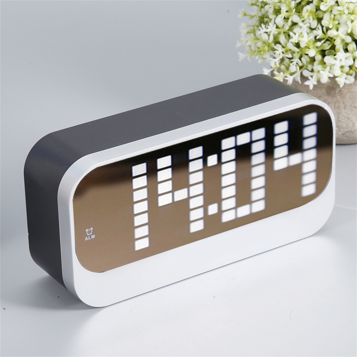 Ein digitaler Wecker, schwarz und silber, zeigt 14:04 an. Der Wecker hat eine rechteckige Form und ein Spiegeldisplay.