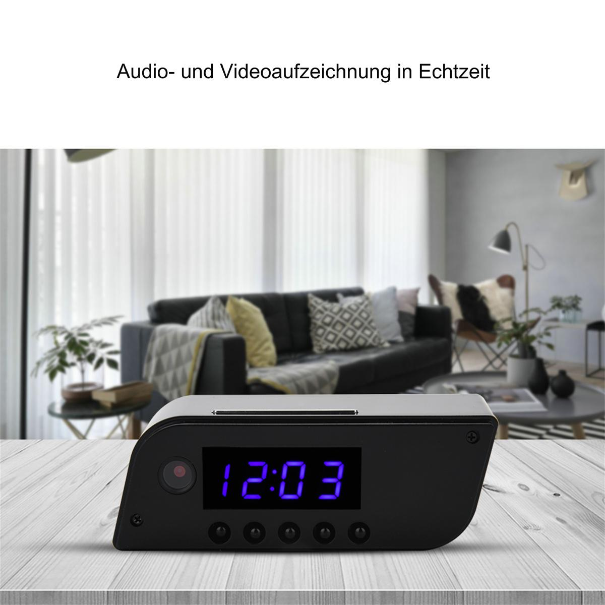Eine schwarze Digitaluhr, die 12:03 anzeigt, mit Knöpfen, auf einem Holztisch. Im Hintergrund ist eine Couch.