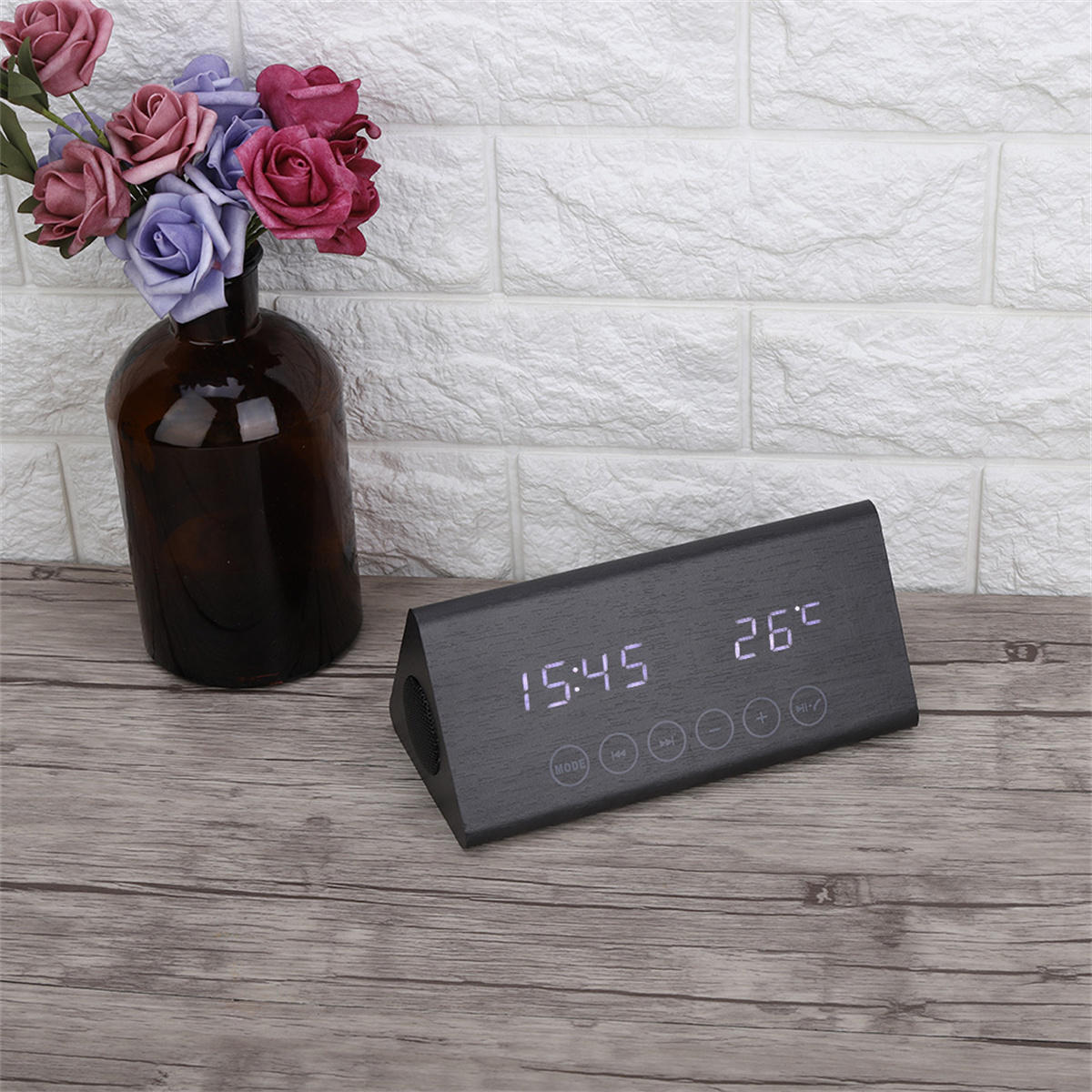 Schwarze Digitaluhr mit Zeit- und Temperaturanzeige, neben einer Blumenvase.