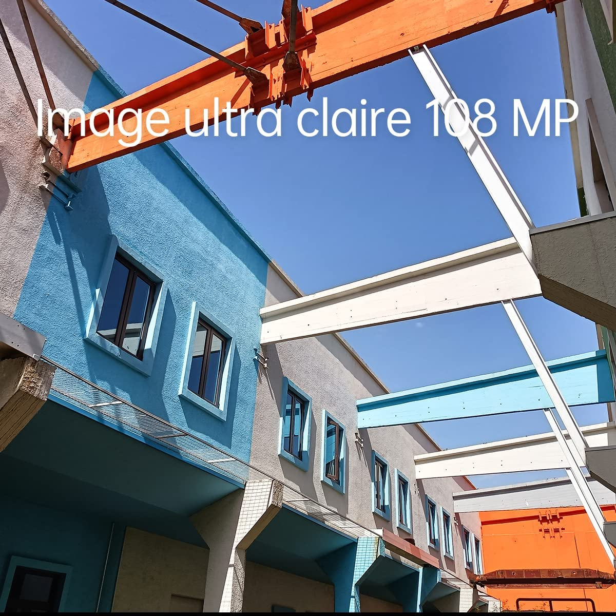Gebäude mit blauen und weißen Wänden unter blauem Himmel. Orange Baumaschinen sichtbar.
