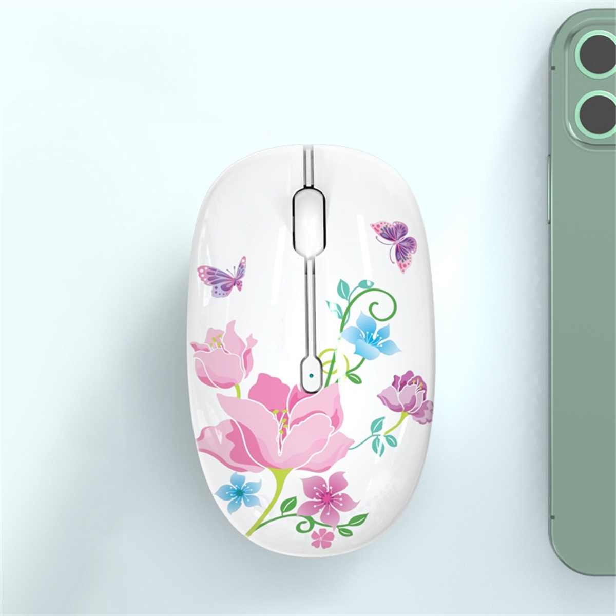 Weiße florale Maus mit Schmetterlingen auf einem Tisch, grünes Telefon daneben.