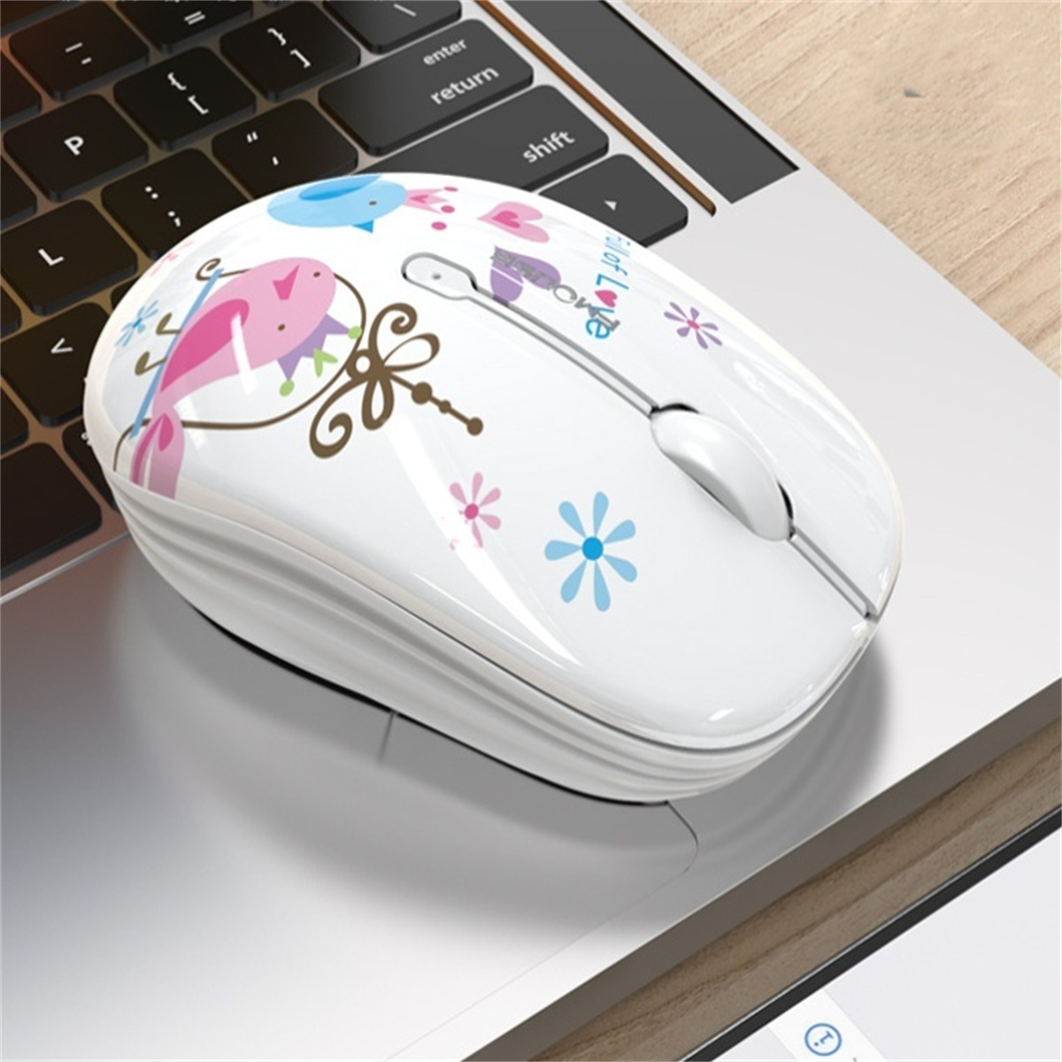 Weiße kabellose Maus mit Blumendesign und Vögeln auf einem silbernen Laptop.