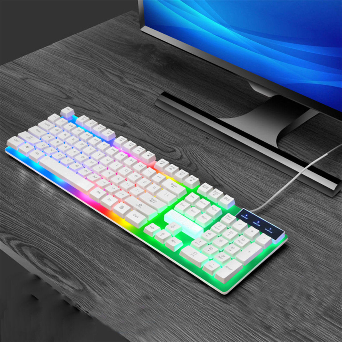 Weiße Gaming-Tastatur mit Regenbogen-LEDs auf einem dunklen Holztisch mit Computermonitor.