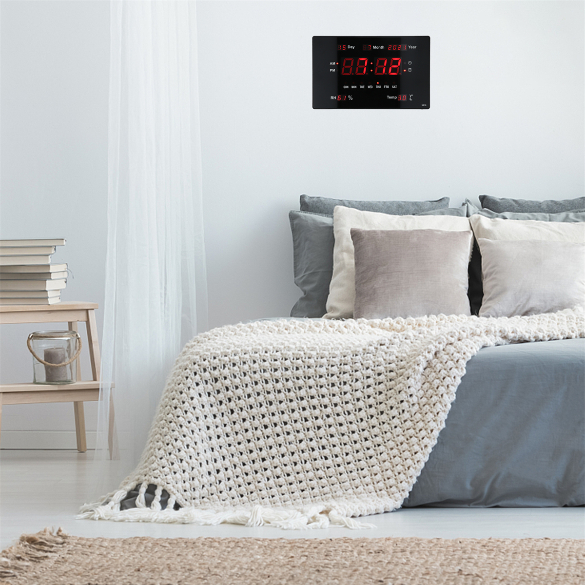 Eine Digitaluhr auf schwarzem Hintergrund über einem Bett. Sie zeigt Zeit, Datum und Temperatur an.