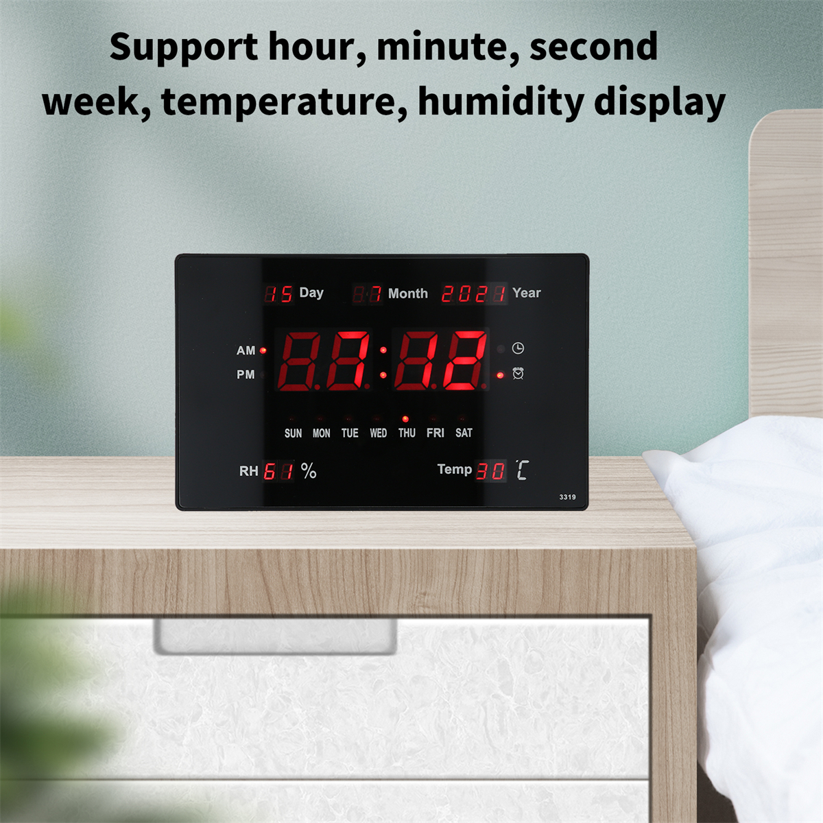 Eine schwarze Digitaluhr zeigt Zeit, Datum und Temperatur. Sie steht auf einem weißen Nachttisch.