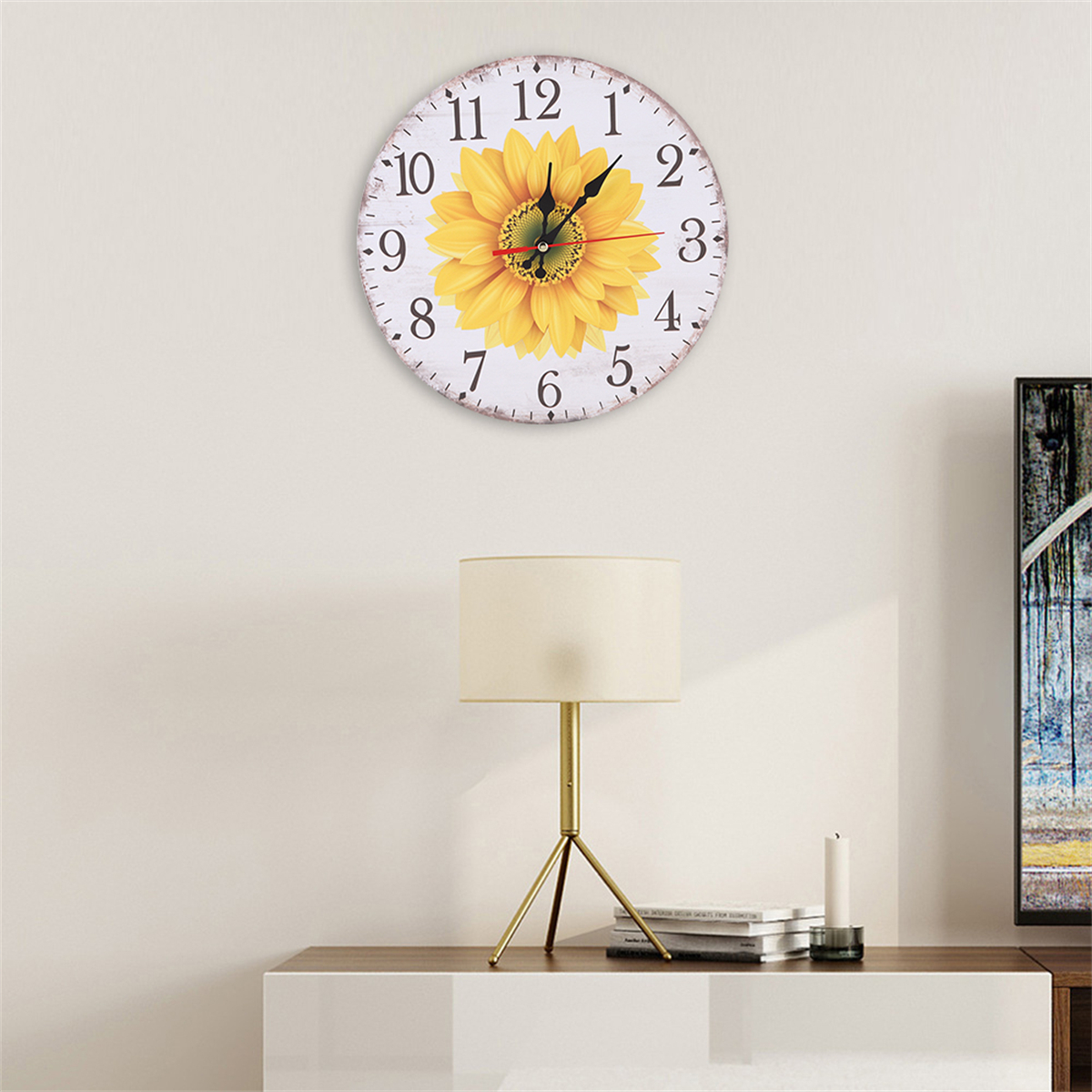 Weiße Uhr mit Sonnenblumenmuster. Die Uhr hängt an einer Wand über einer Lampe und einem weißen Schrank.