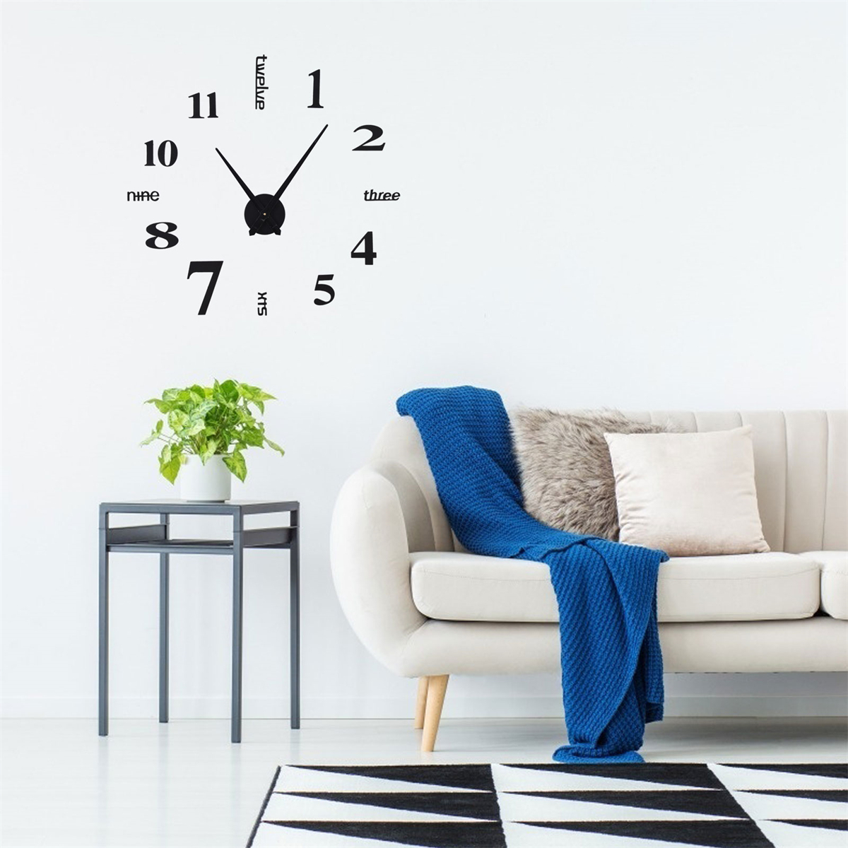 Eine Wanduhr mit schwarzen Zahlen und Zeigern, über einem Sofa und Dekoration.