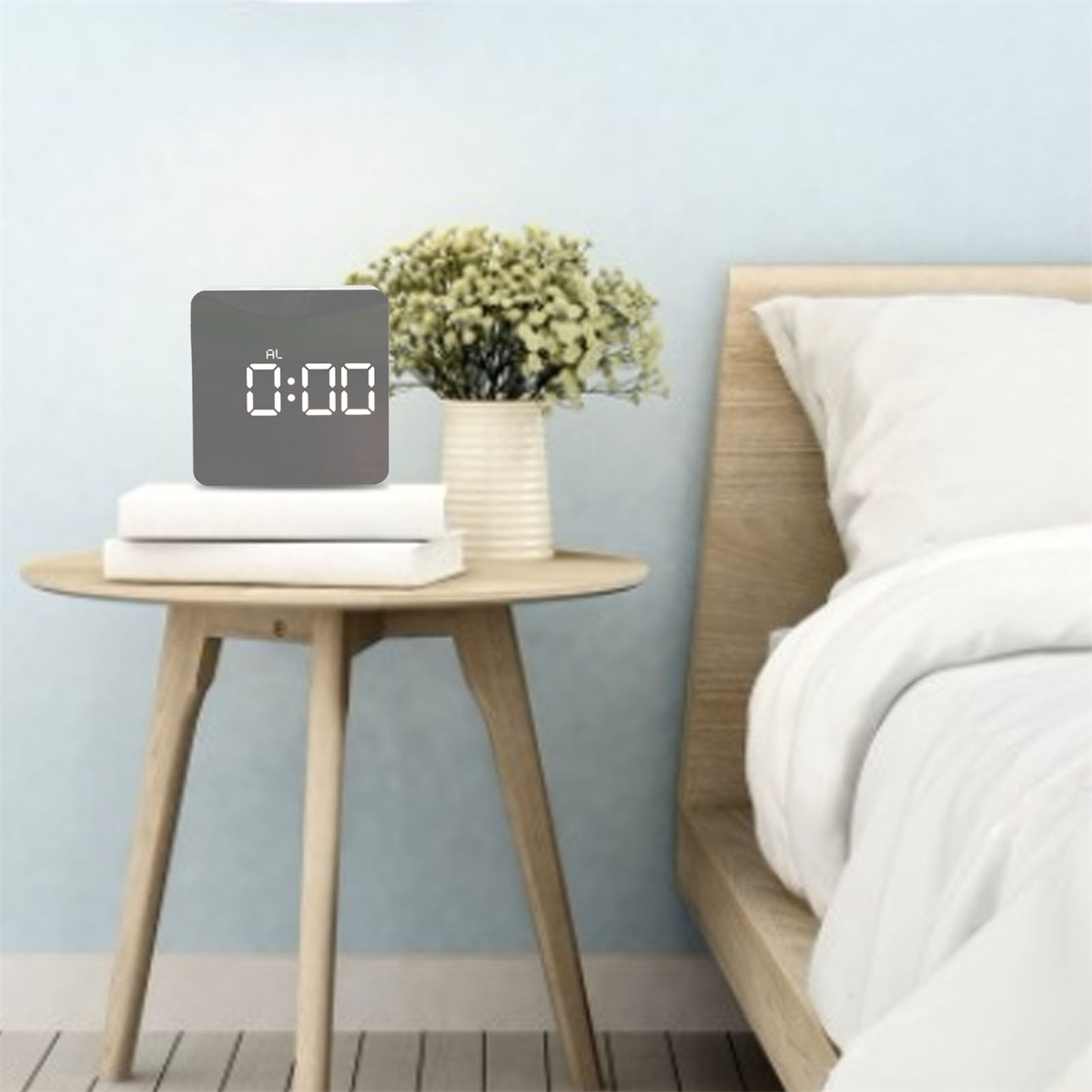 Digitaluhr auf einem Tisch mit Büchern und einer Blumenvase. Bett im Hintergrund. Hellblaue Wand.