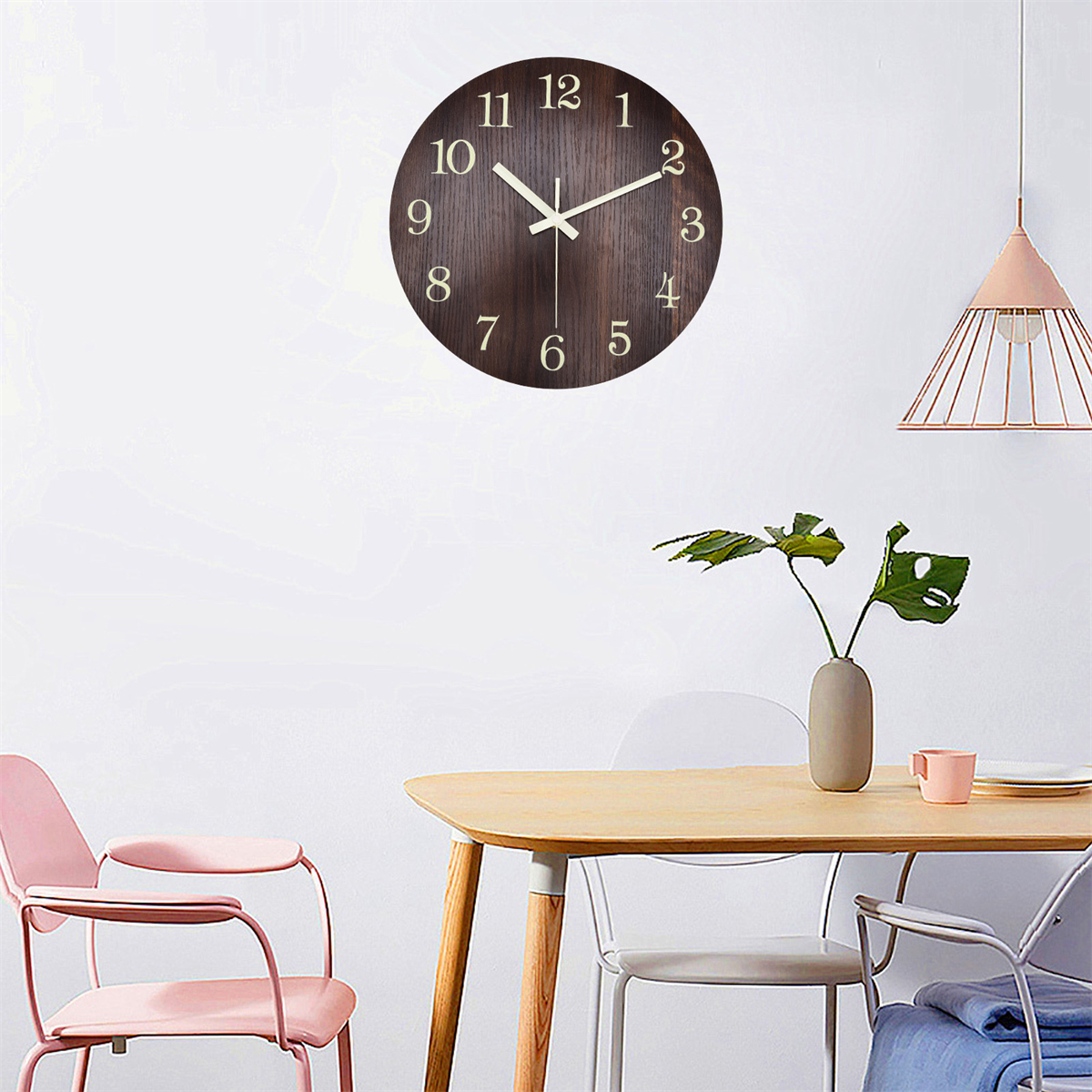 Hölzerne Wanduhr mit hellen Zahlen. Tisch mit Pflanze und rosa Stuhl.