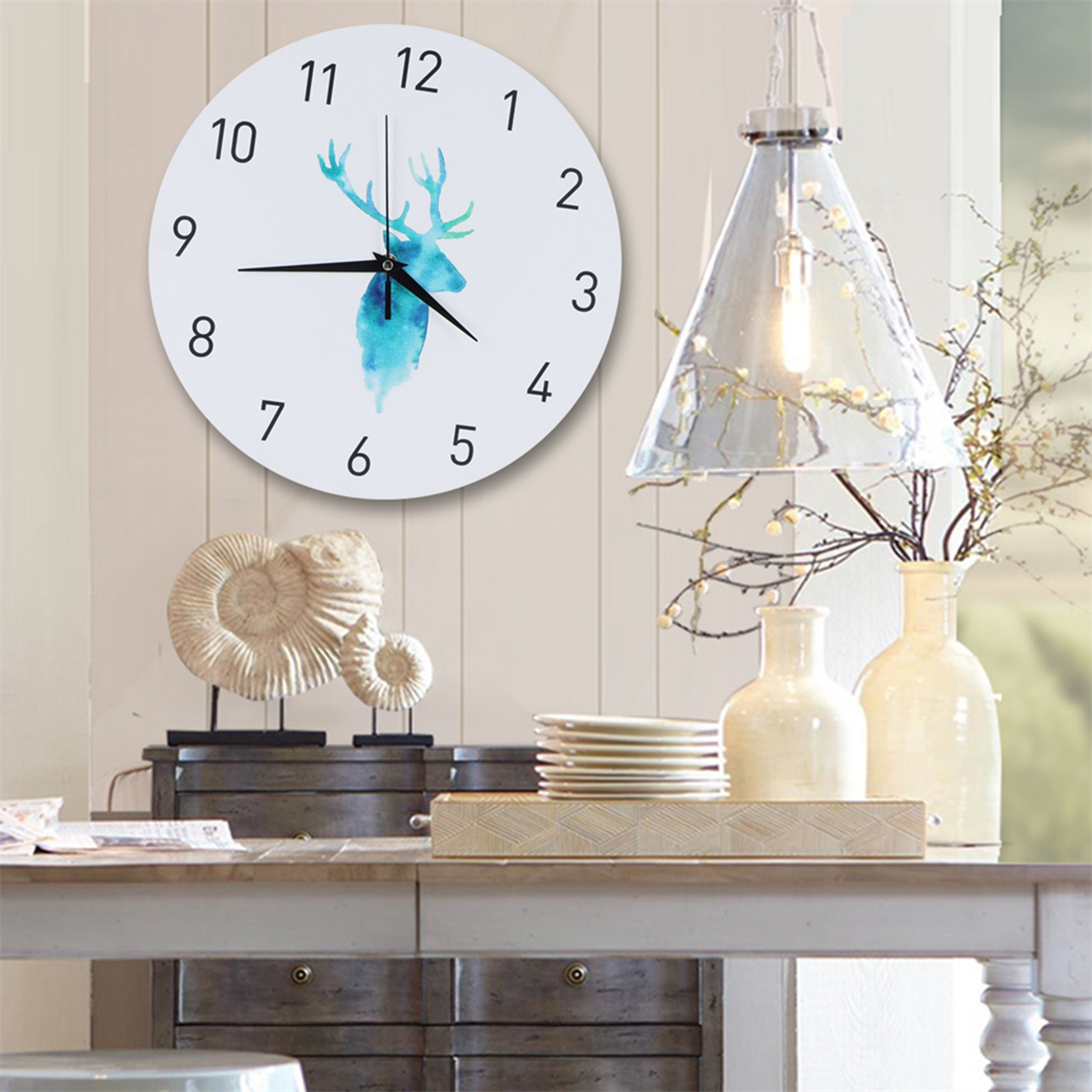 Eine weiße Uhr mit einer blauen Hirschsilhouette, die an einer Wand mit Dekoration hängt.