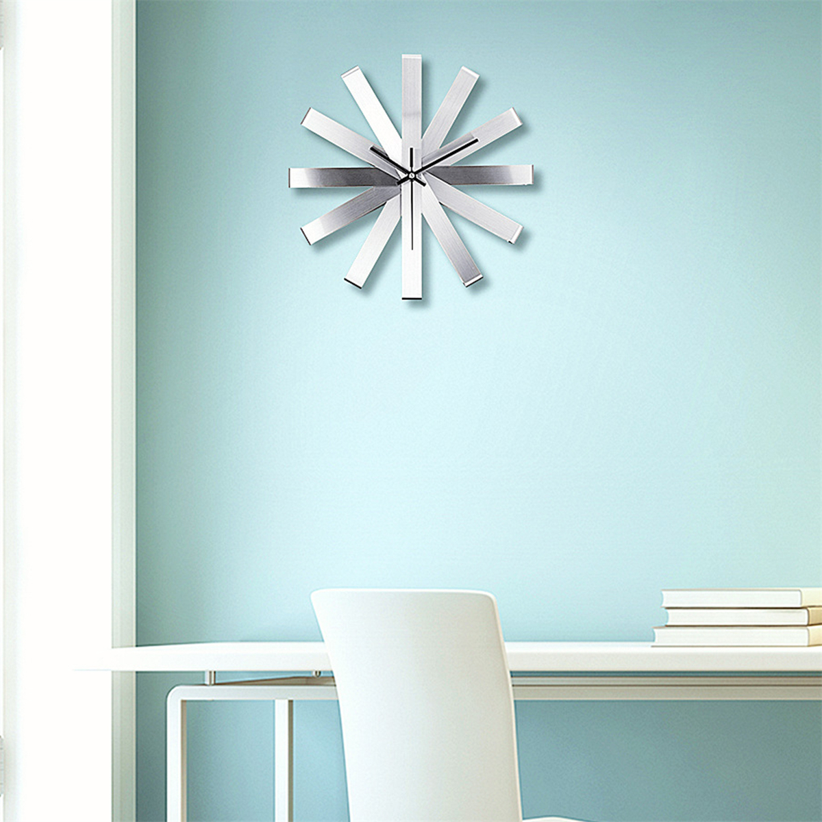 Moderne silberne Uhr an einer hellblauen Wand. Weißer Schreibtisch und Stuhl sind im Bild.
