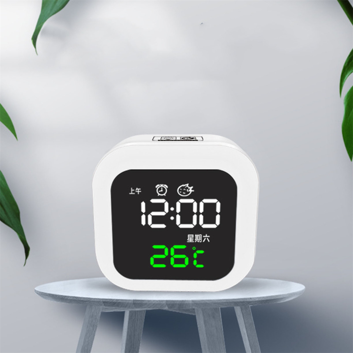 Weißer digitaler Wecker mit Anzeige 12:00 und 26°C, auf einem Tisch.
