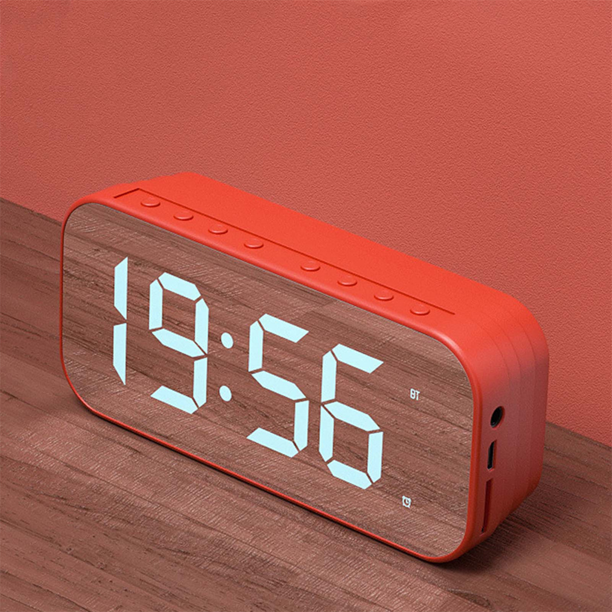 Roter digitaler Wecker mit der Anzeige 19:56. Er steht auf einem Holztisch, im Hintergrund eine rote Wand.